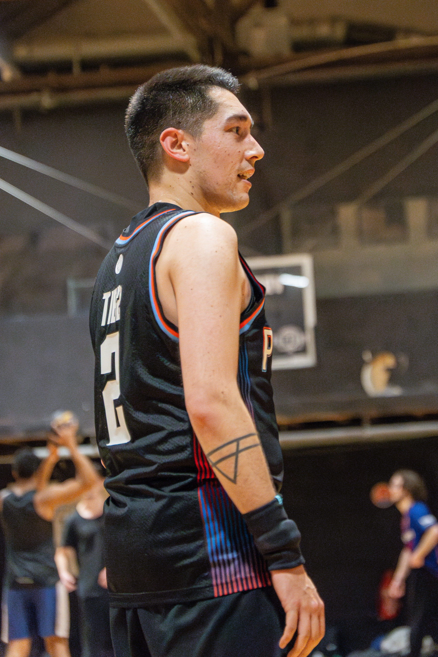 A basketball player wearing a black jersey with the number 2 is standing on a court with other players in the background.