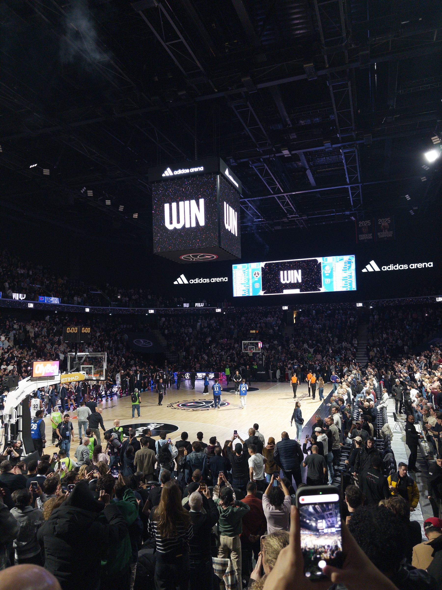 A basketball game has just concluded in a large stadium filled with spectators, with the scoreboard displaying WIN.