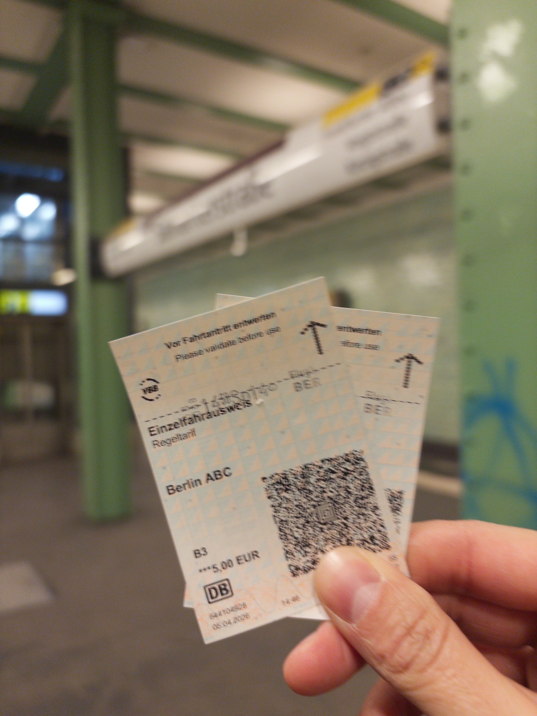 Auto-generated description: A hand is holding three printed subway tickets at a train station platform.