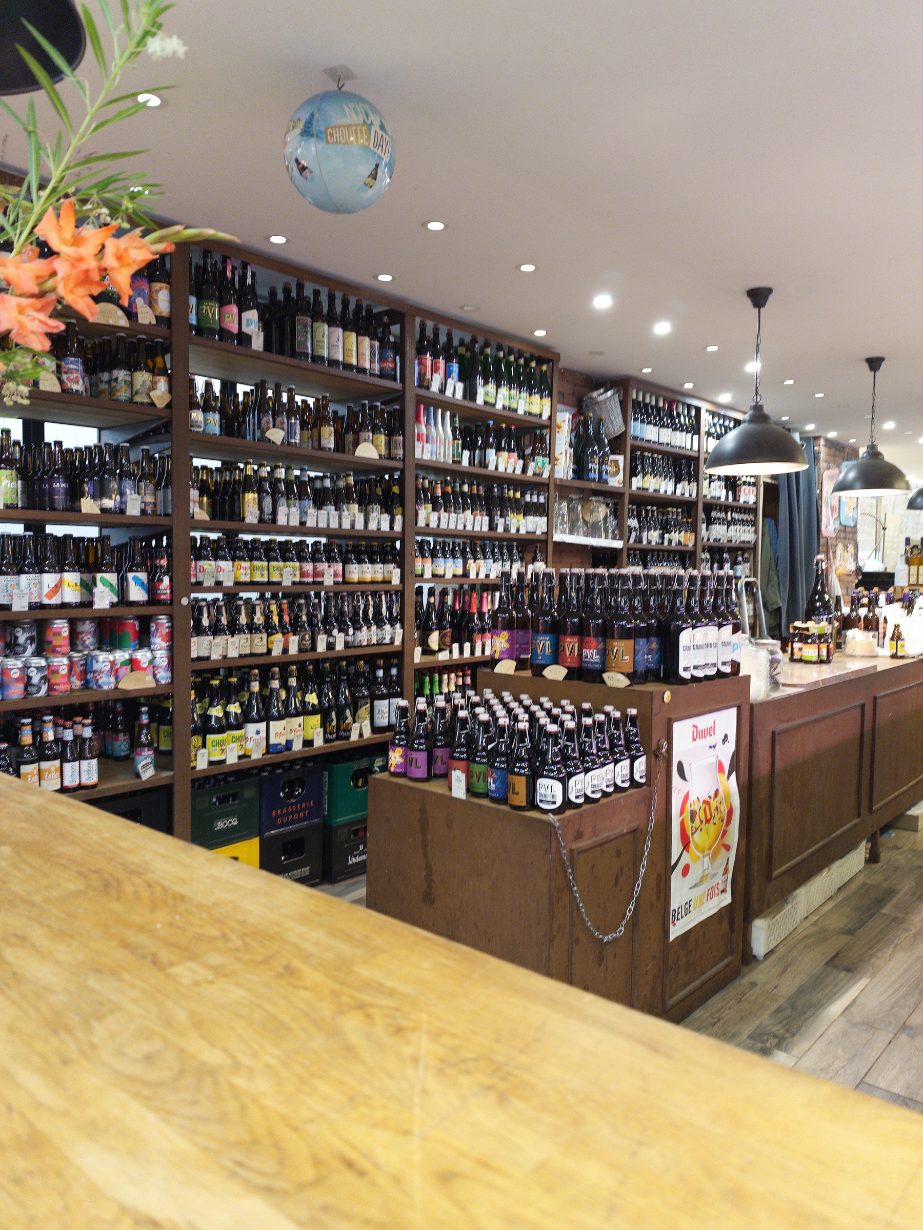 A well-stocked bar or liquor store interior features numerous shelves filled with bottles of beer and other alcoholic beverages, with additional bottles displayed on a wooden counter.