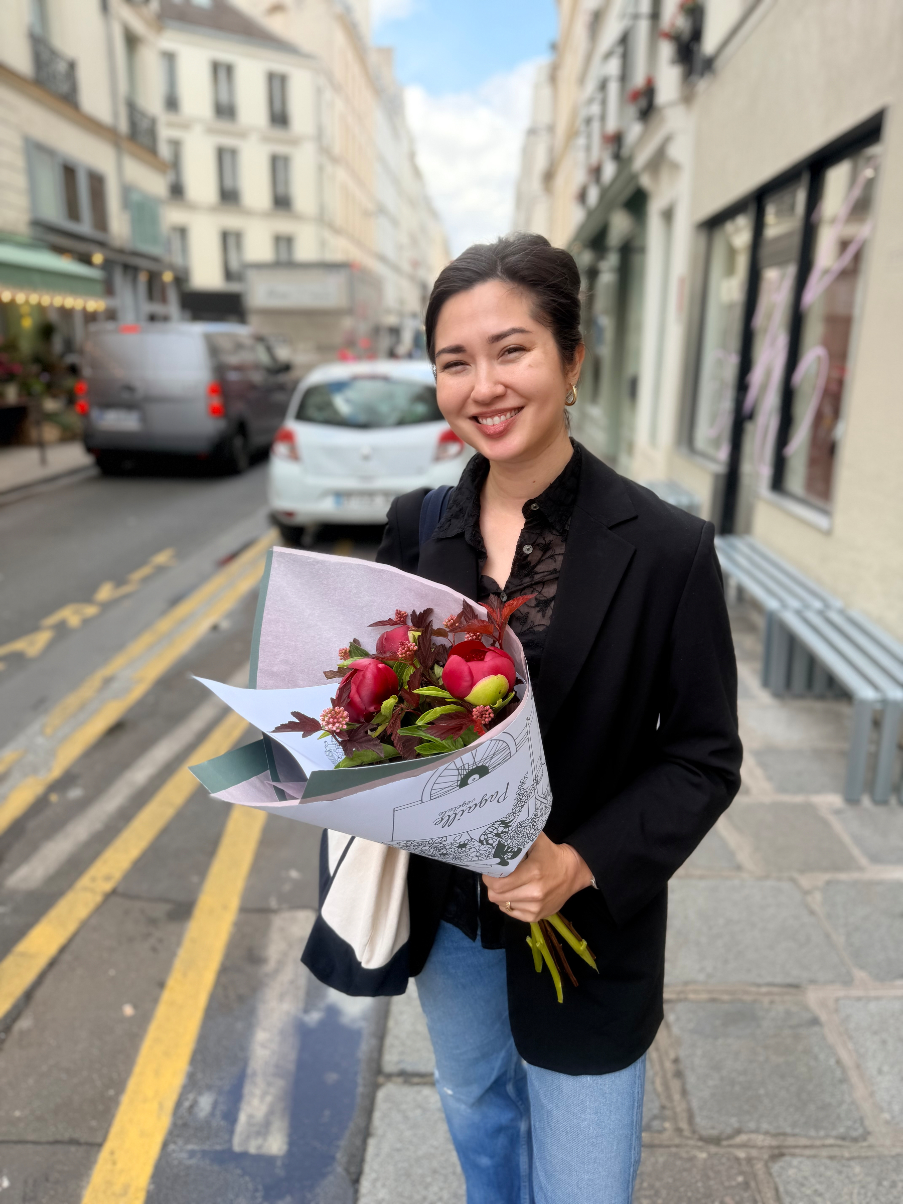 Auto-generated description: A person is standing on a street holding a bouquet of flowers and smiling.