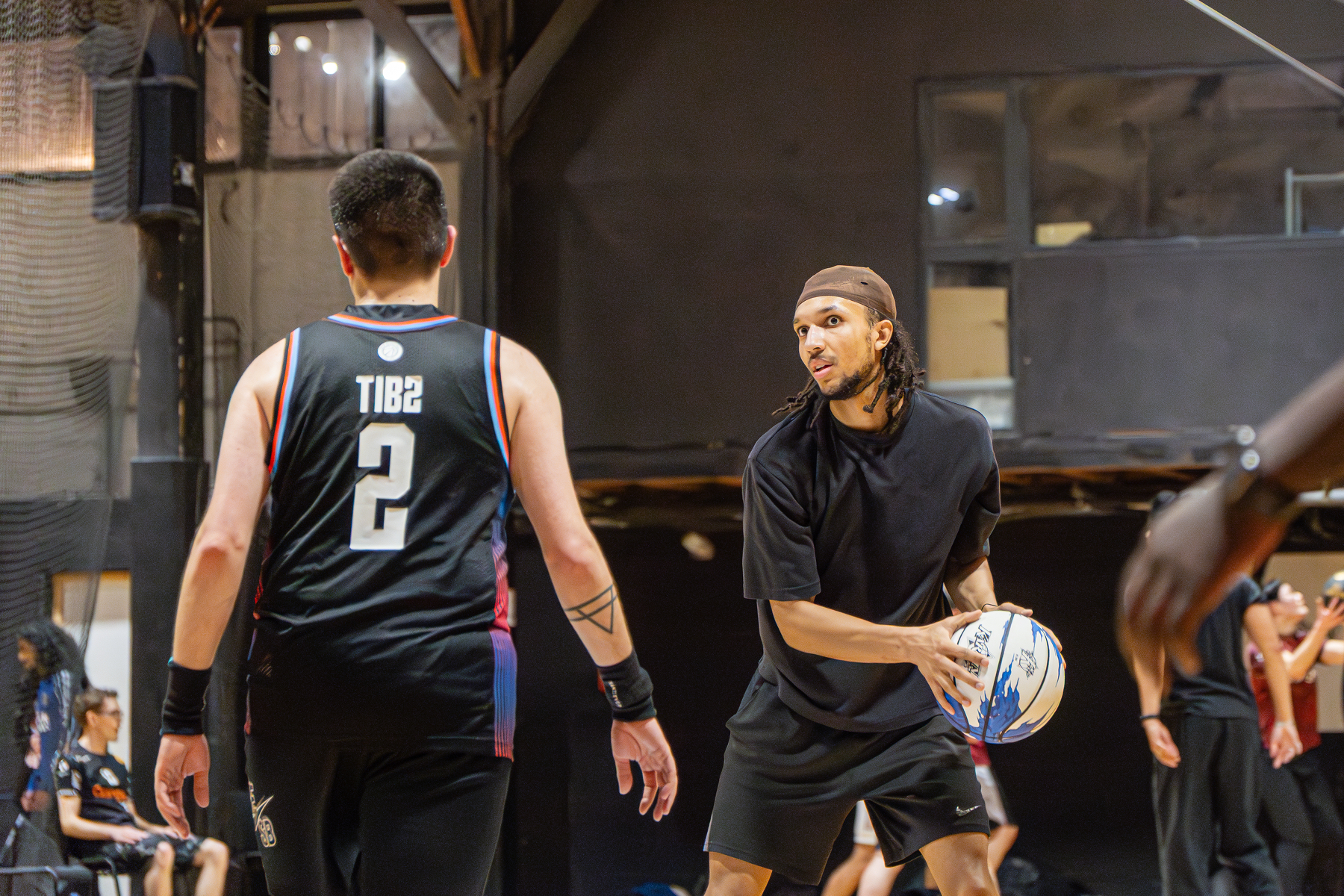 A basketball player in a black outfit prepares to pass the ball while being guarded by another player wearing a jersey with the number 2.
