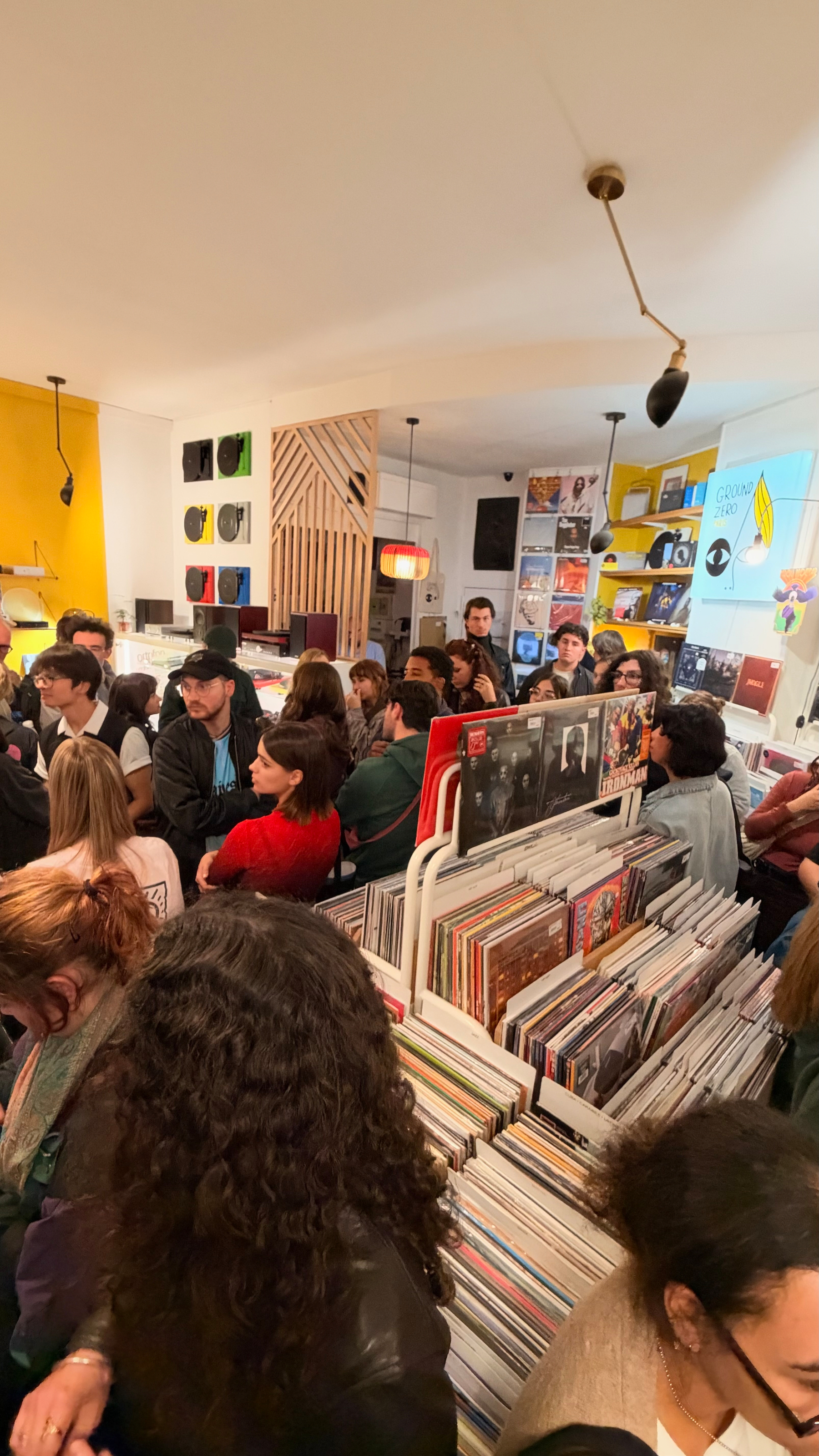 A crowded record store with people browsing through vinyl records and socializing in a brightly lit, colorful interior.