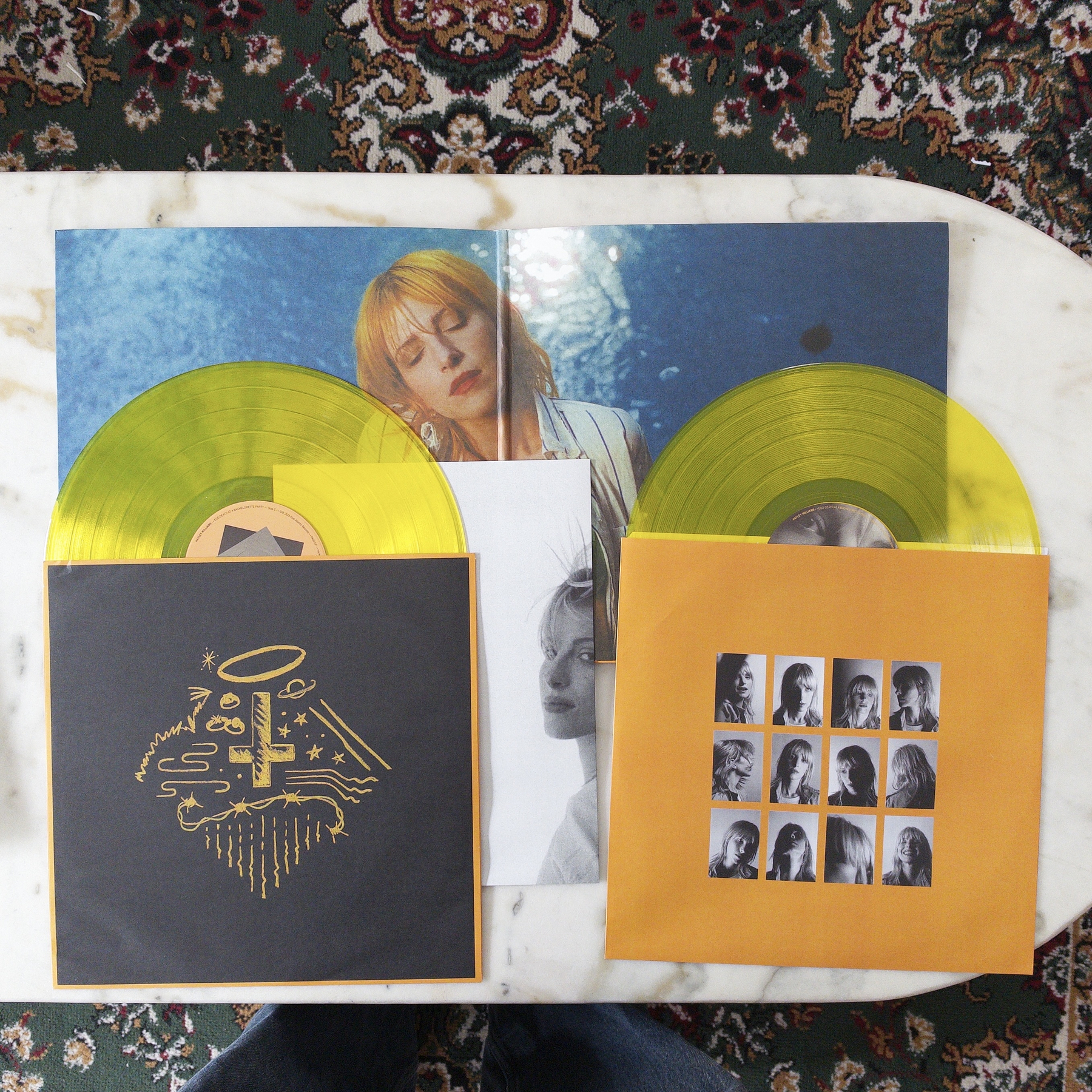 Two yellow vinyl records (Ego Death at the Bachelor Party by Hayley Williams) are partially pulled out from their respective sleeves, which are placed on a marble surface alongside an album cover featuring a woman with reddish hair and an inner black-and-white photograph.
