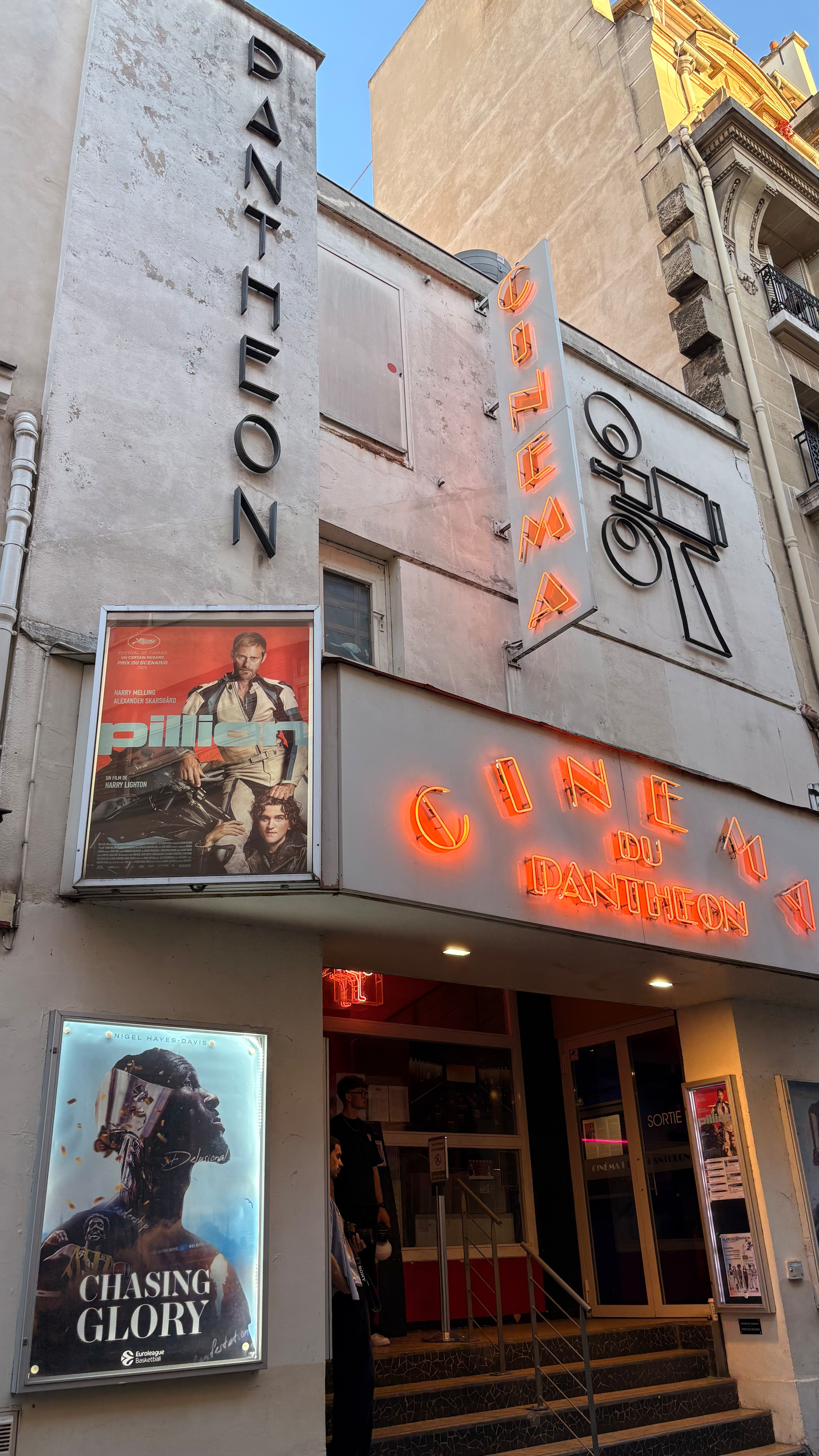 A vintage cinema entrance displays neon signs and posters for the film Chasing Glory.