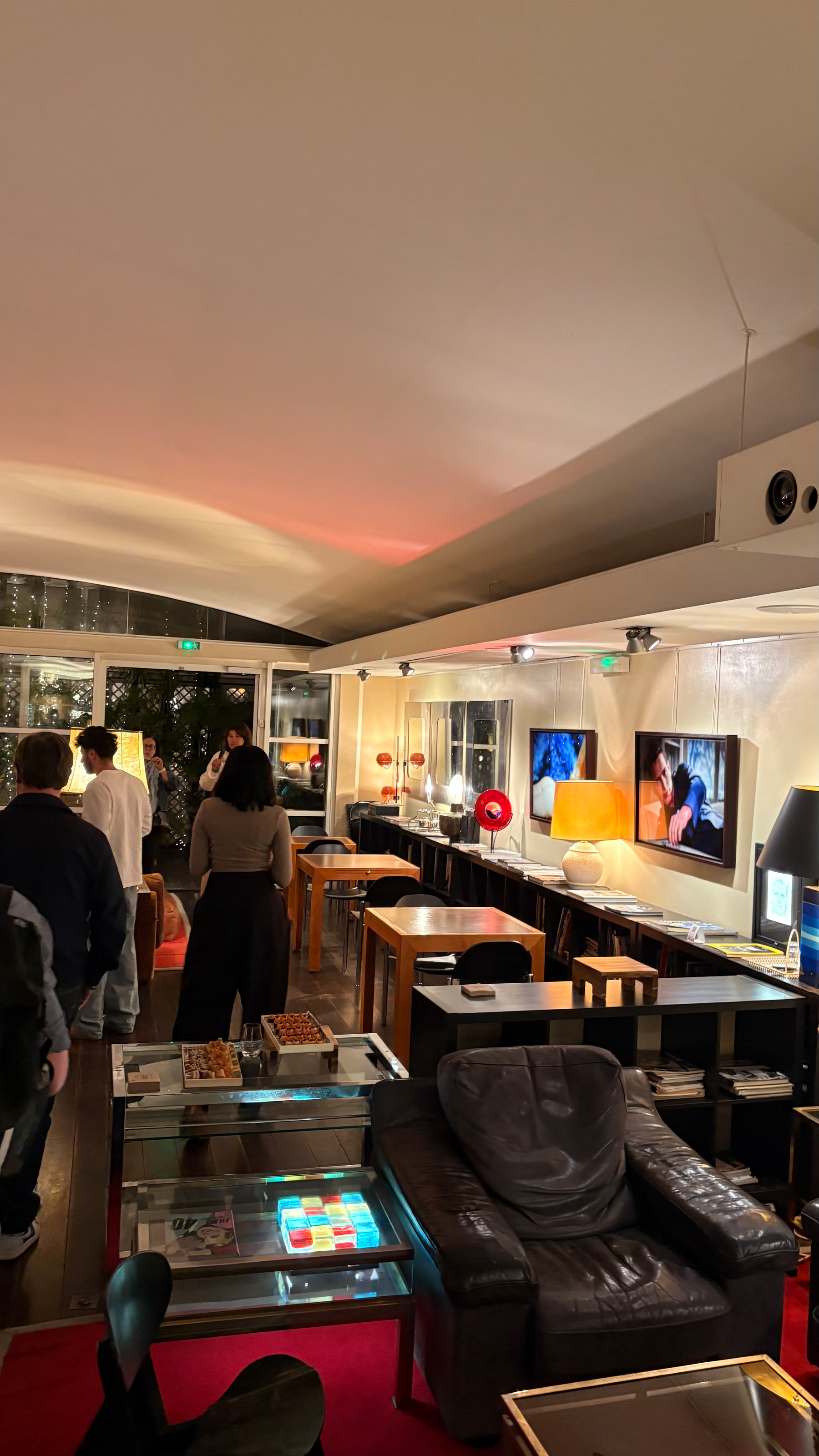 A modern lounge features various colorful lamps, contemporary furniture, and people casually gathering around.