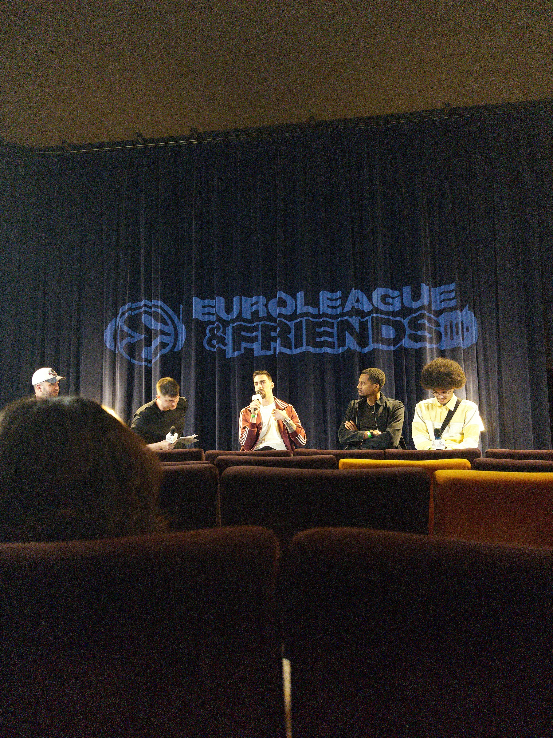 Five people are seated on stage with the Euroleague & Friends logo projected on a curtain behind them.