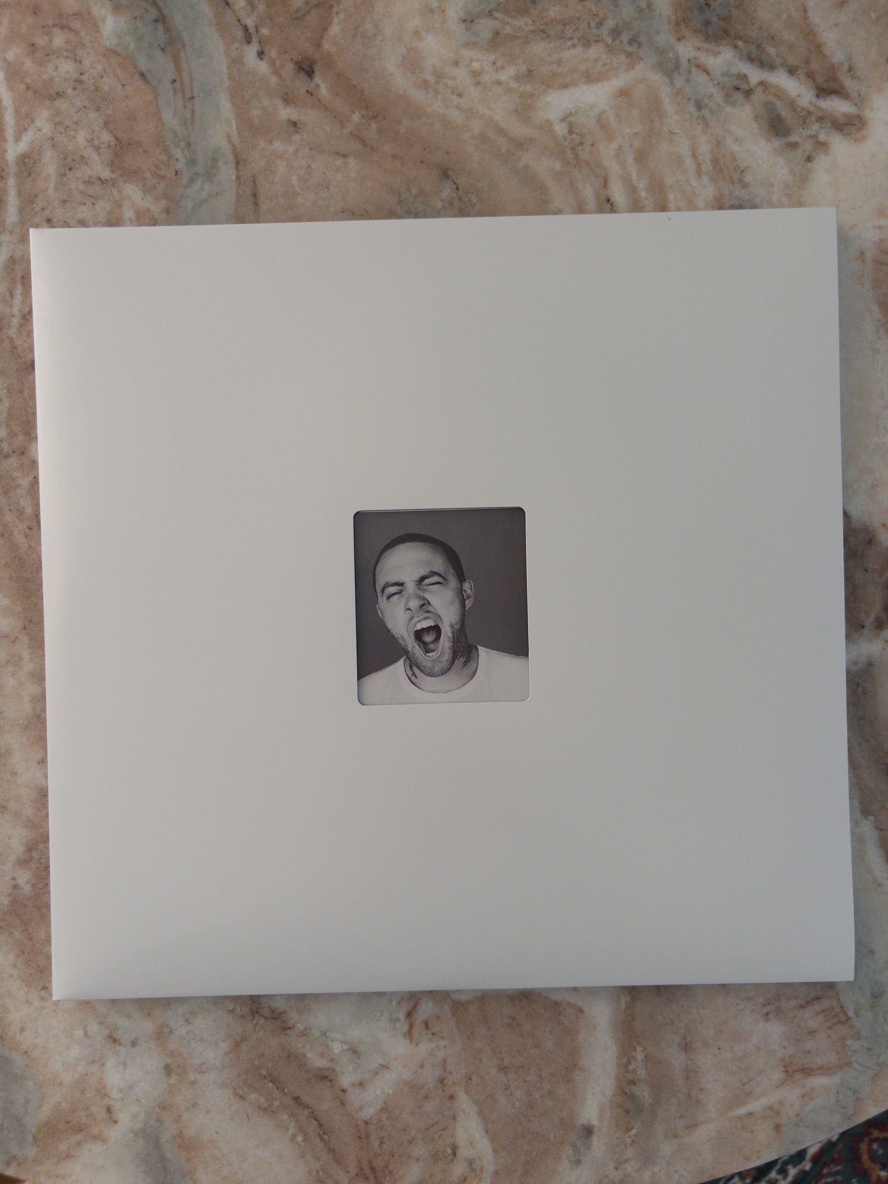 A square white album cover features a small black-and-white photo of a man yawning centered on it.
