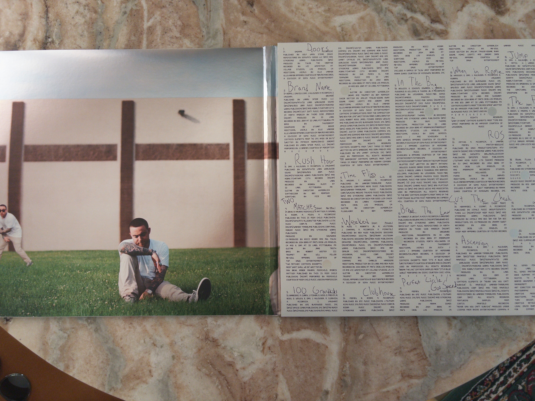 An open album displays a photo of a man sitting on grass against a building wall on the left page, while the right page contains handwritten notes or lyrics.