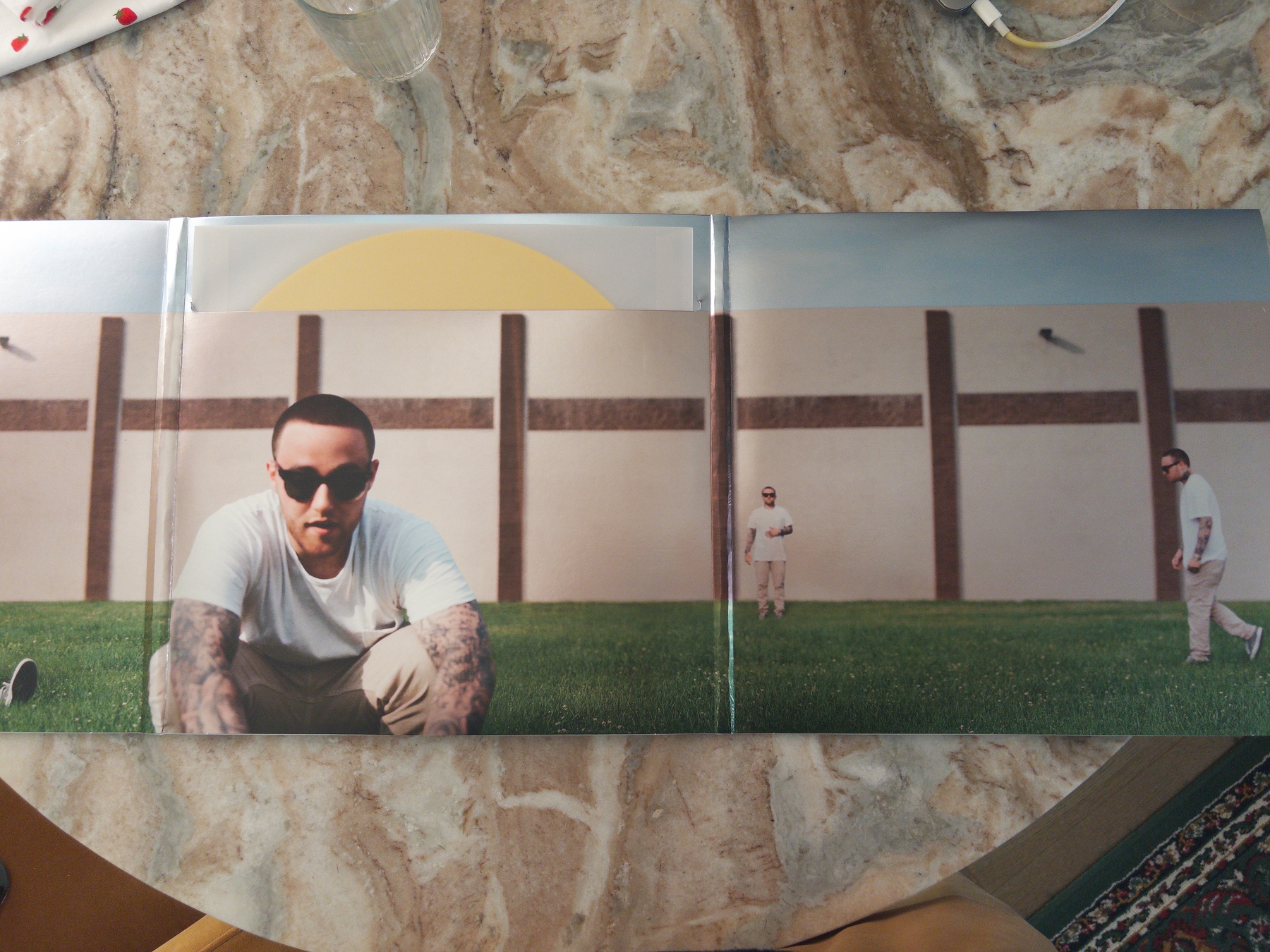 A vinyl record cover features a panoramic photo of a man in a white shirt and sunglasses appearing three times in different poses on a grassy field in front of a beige wall.