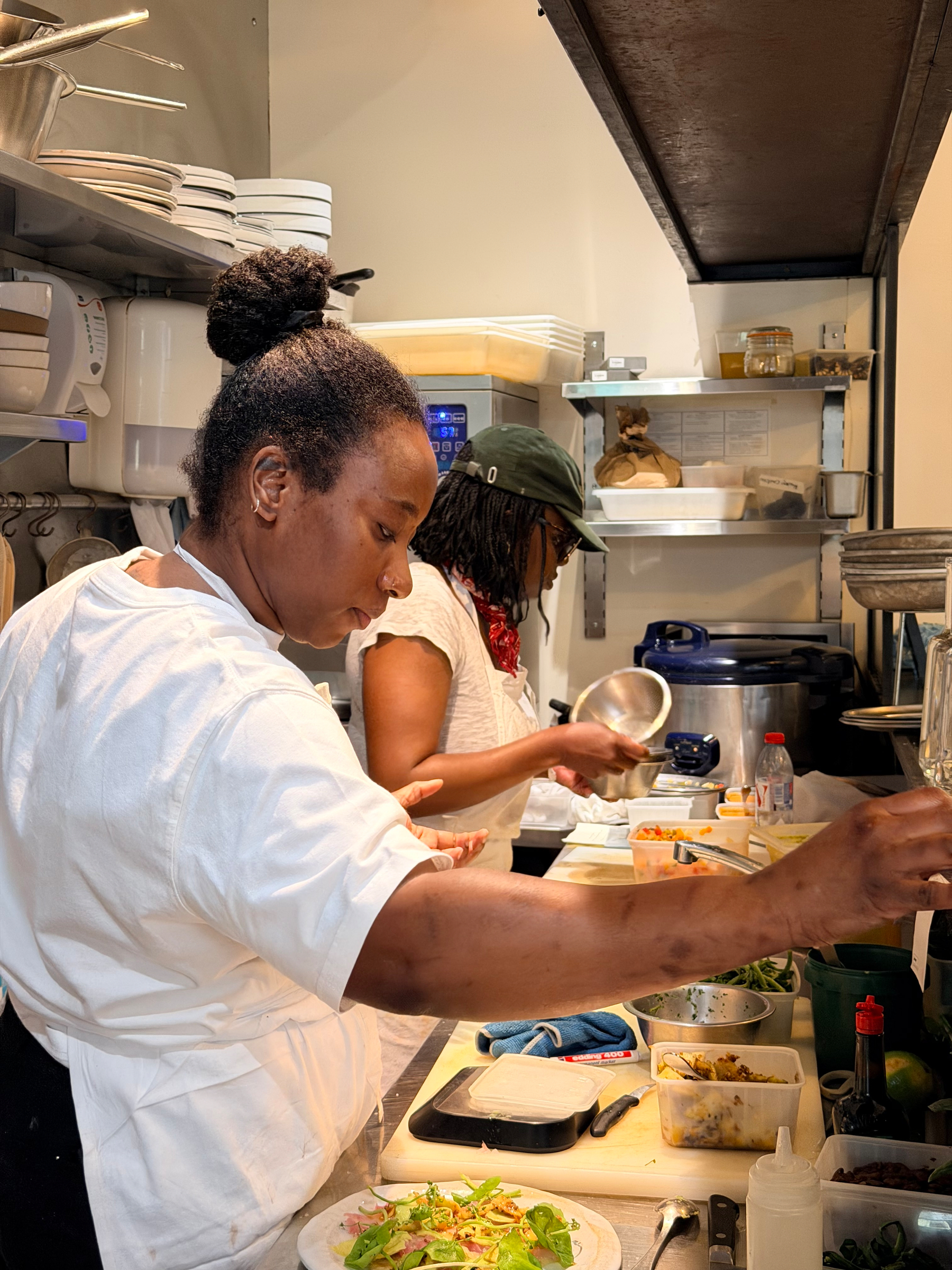 Two people are preparing food in a kitchen, surrounded by various ingredients and kitchenware.