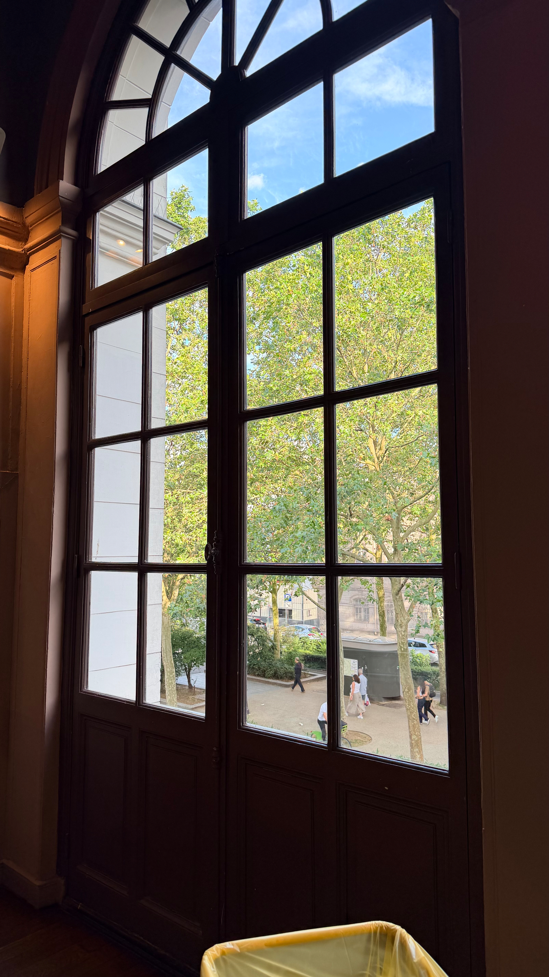 A large arched window reveals a view of people walking by trees outside.