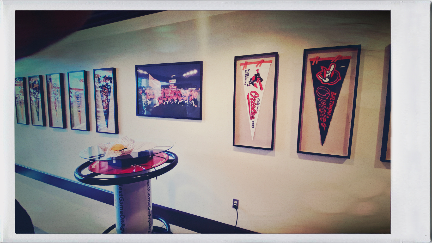 A series of framed sports memorabilia and photographs are displayed on a wall above a small round table with plates and food.