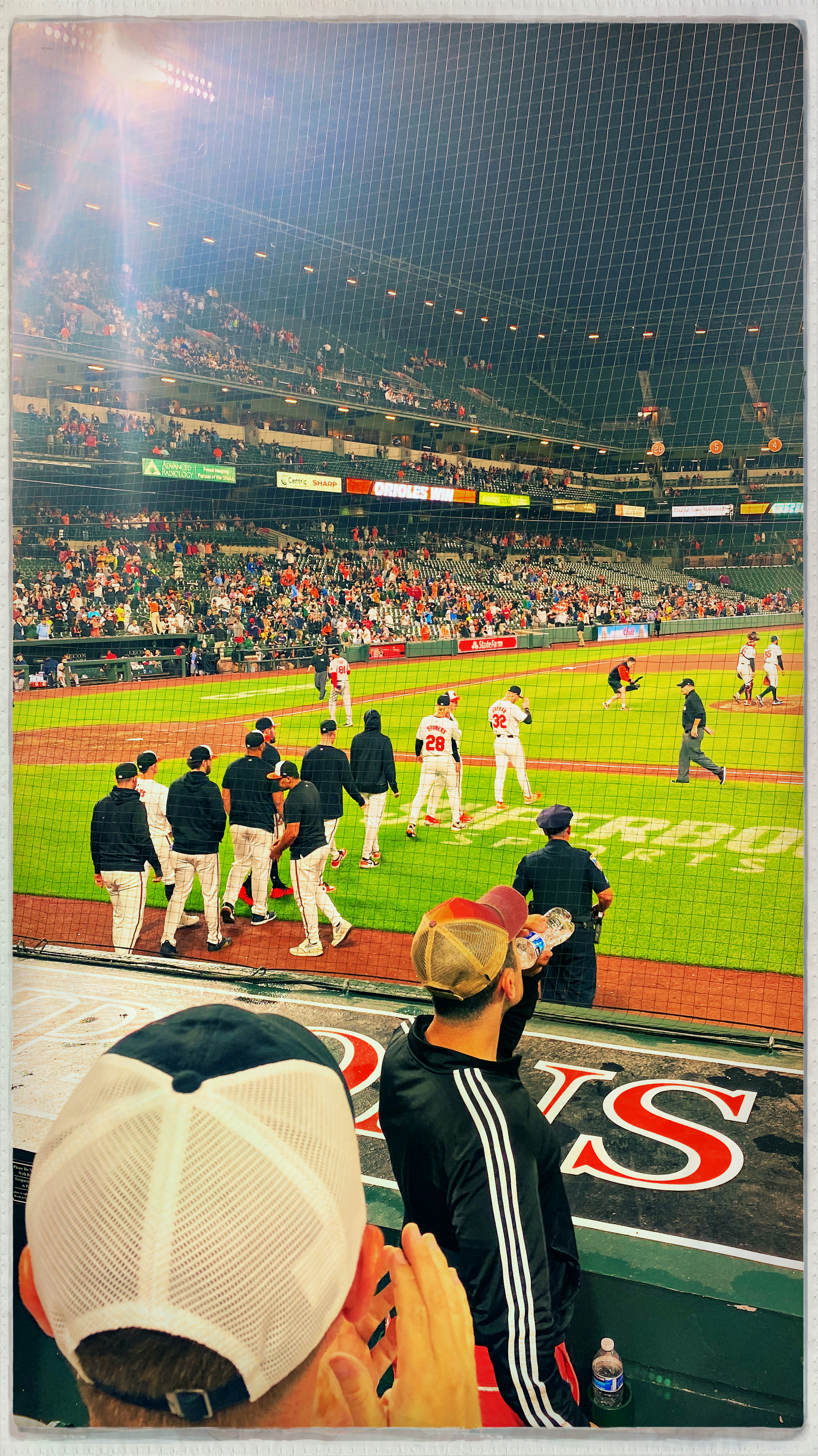 People are watching a baseball game as players and team staff gather on the field, with a lively crowd in the stands.