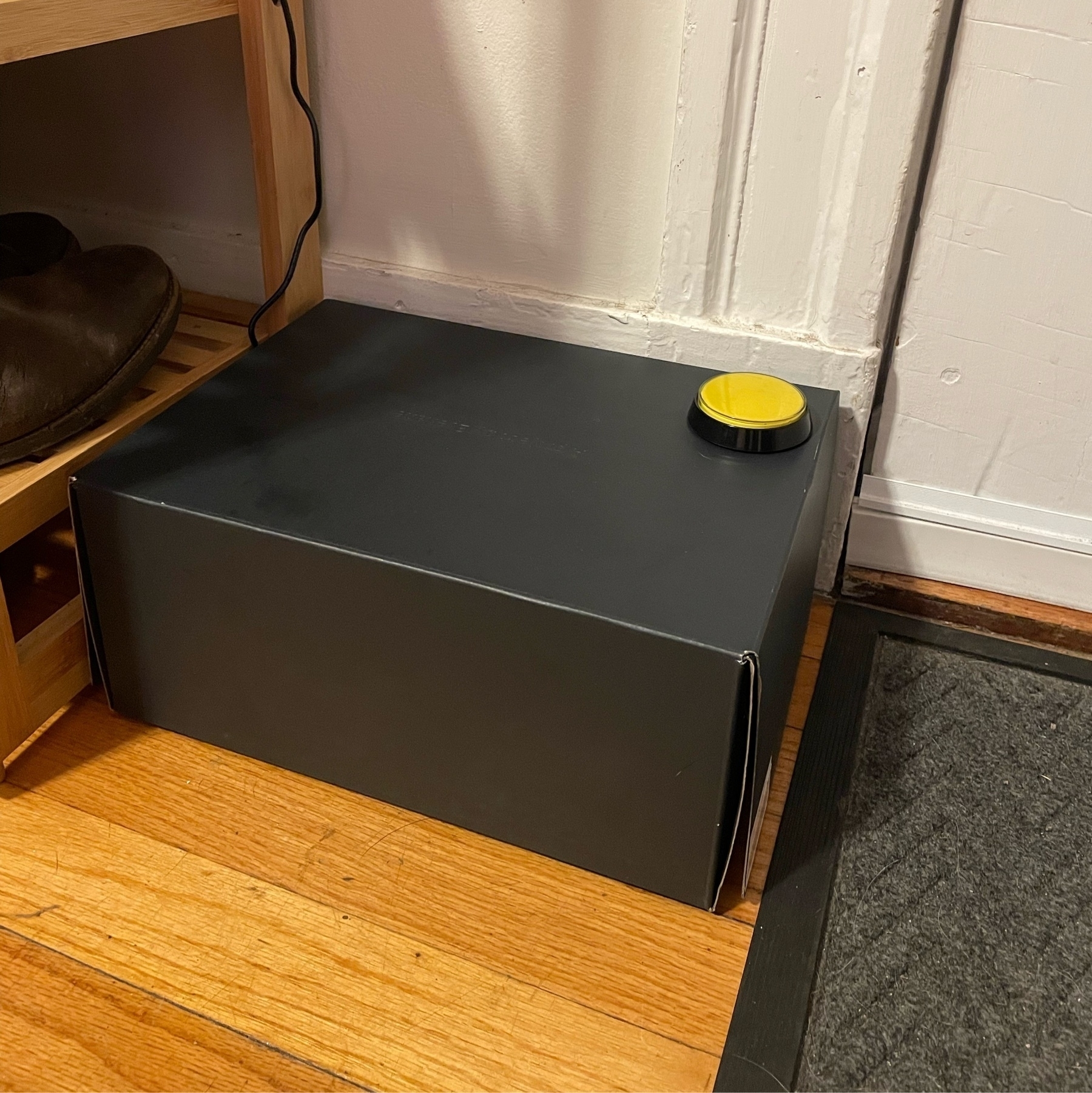 dark shoebox with a yellow button on it sitting next to a door.
