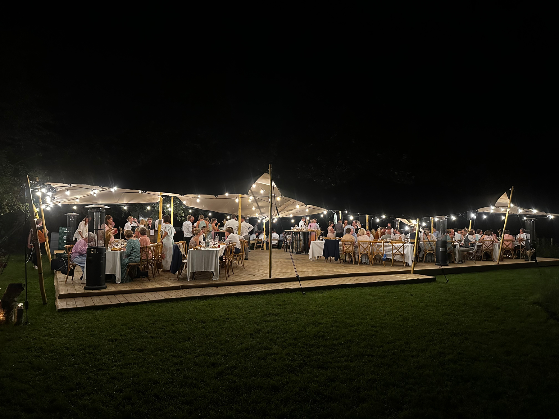 A large white, open tent, beautifully decorated with lights in a dark night