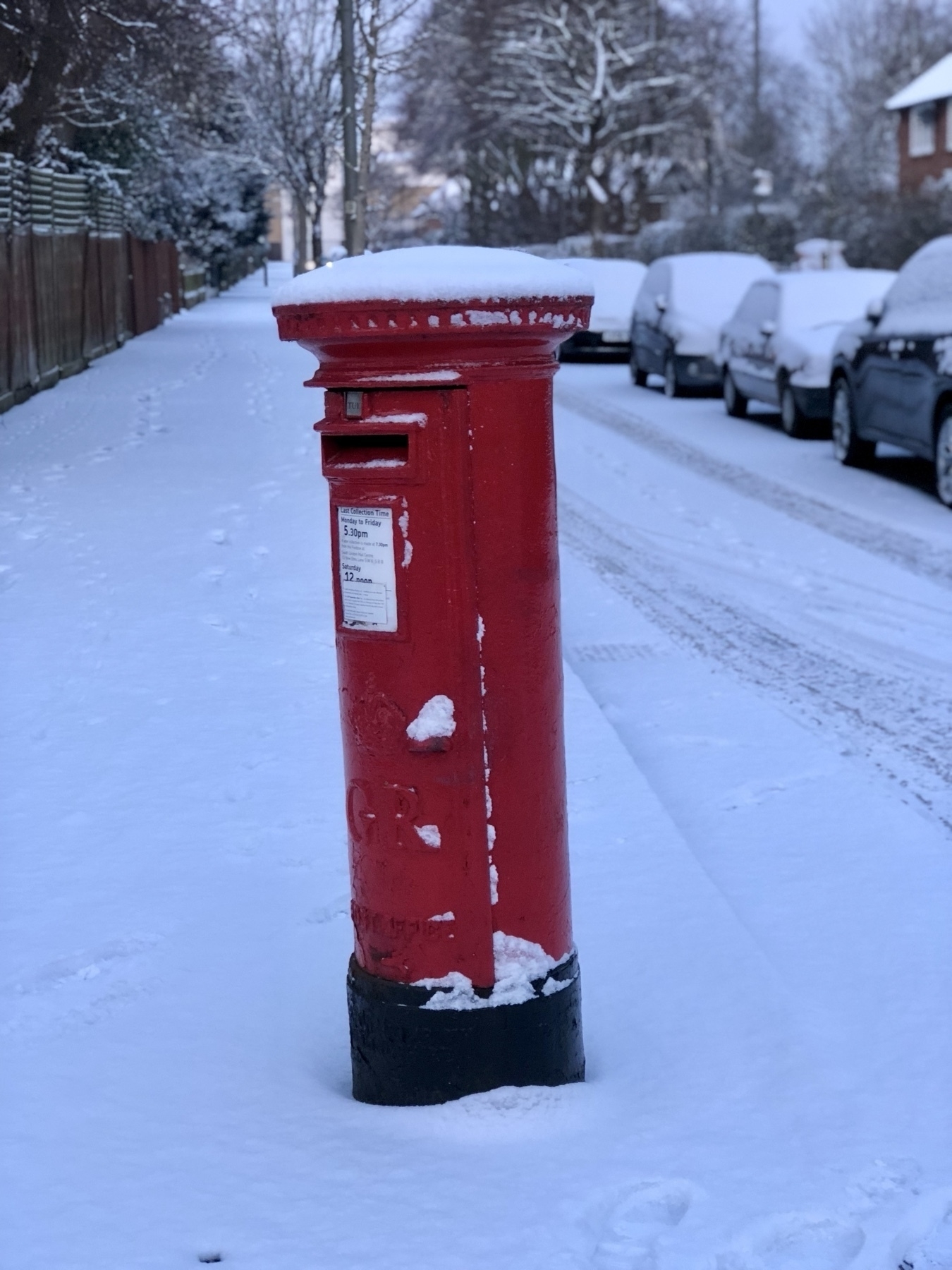 a royal mail postbox wearing a snow cap kn a snowy street