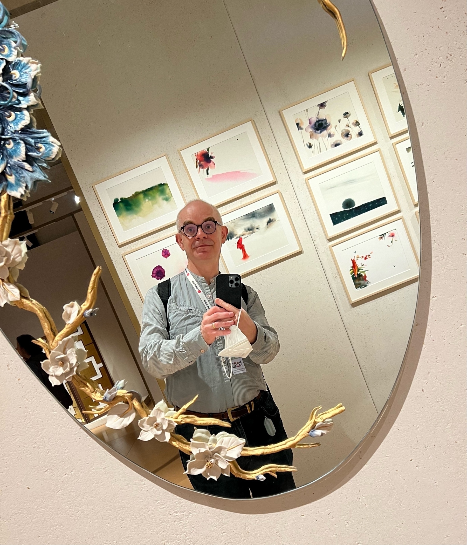 an oval mirror decorated with branches, showing myself and some paintings on the wall 