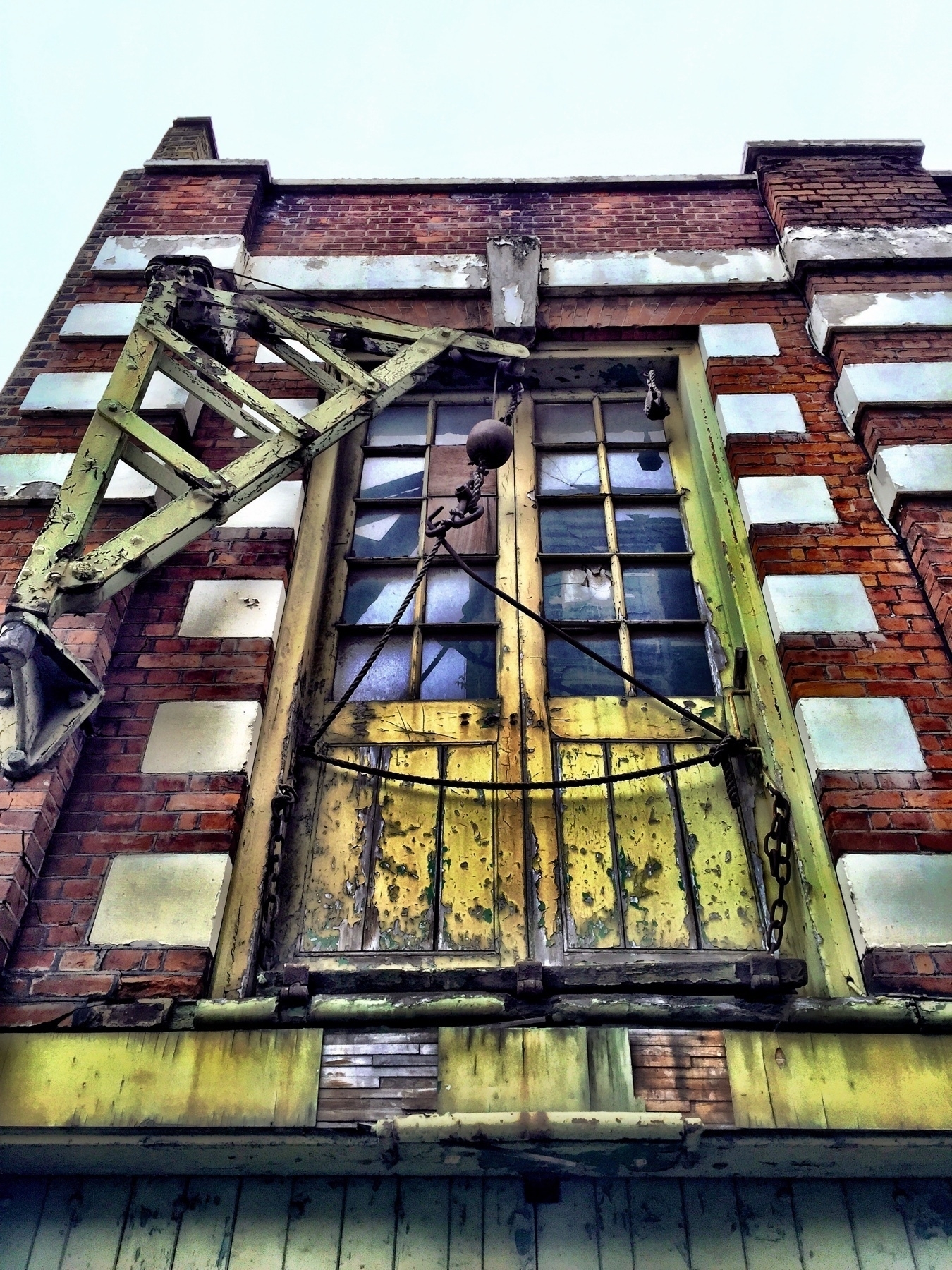 A warehouse door on the first floor of a buliding with a derelict cargo crane next to it