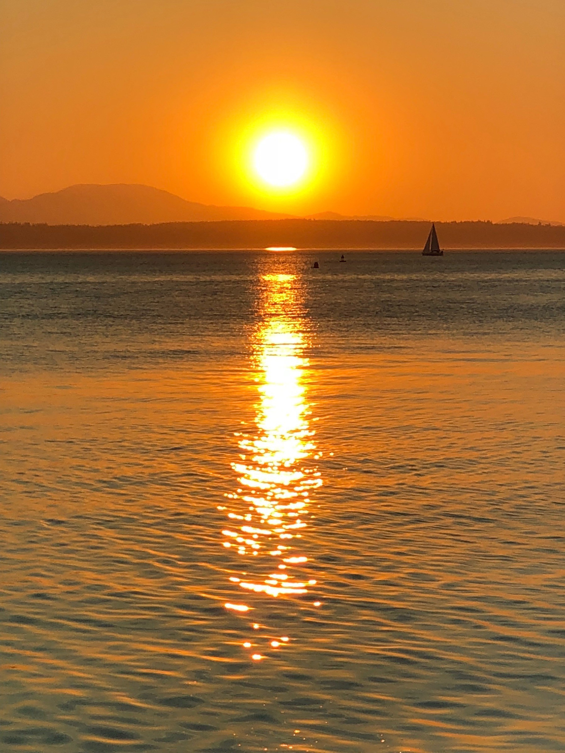 The sun is setting over the Olympics. There are sailboats in Puget Sound.