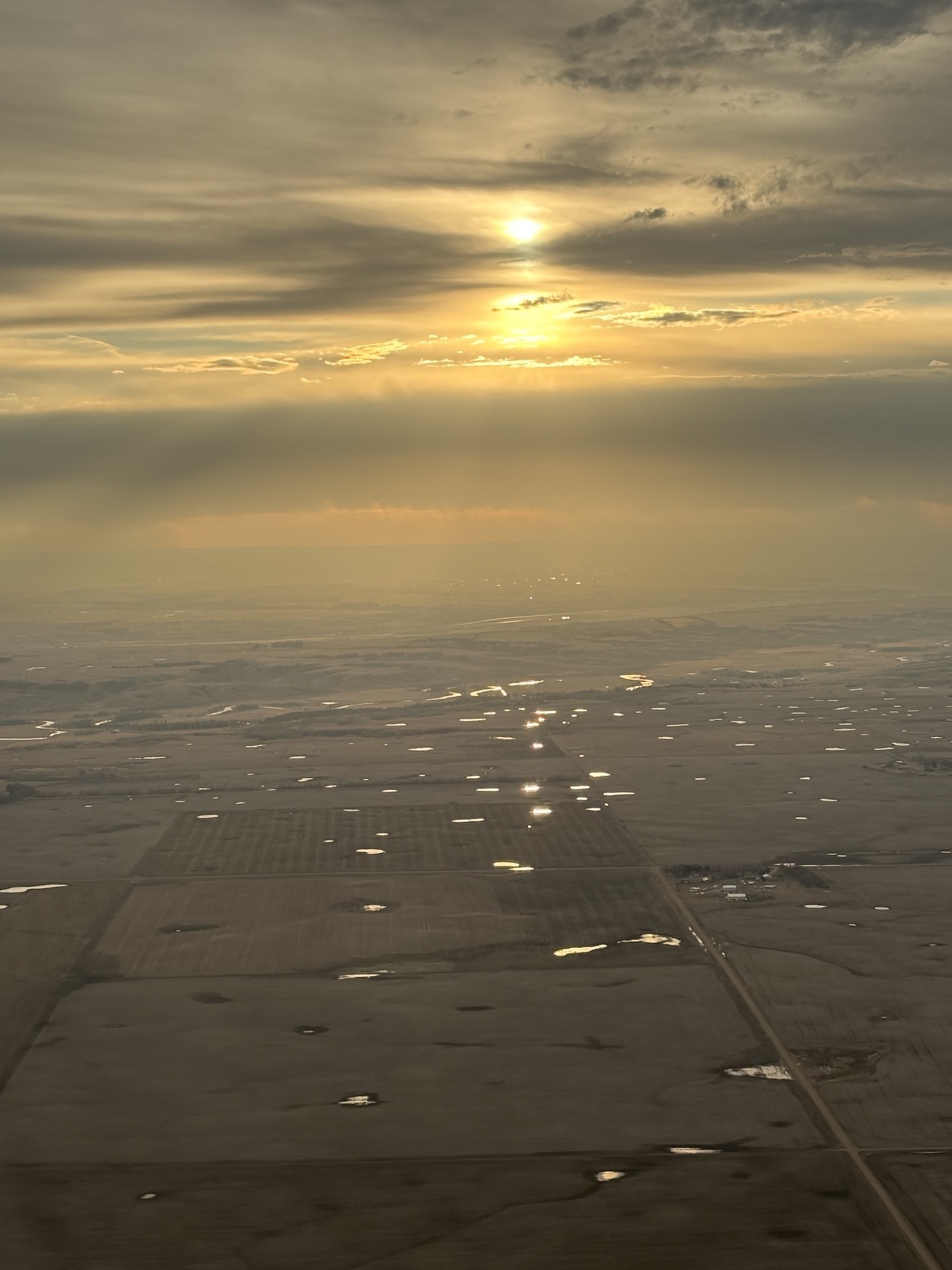 View of North Dakota from the airplane window right before landing in Minot. Sunset and brown landscape with many small sloughs of water.