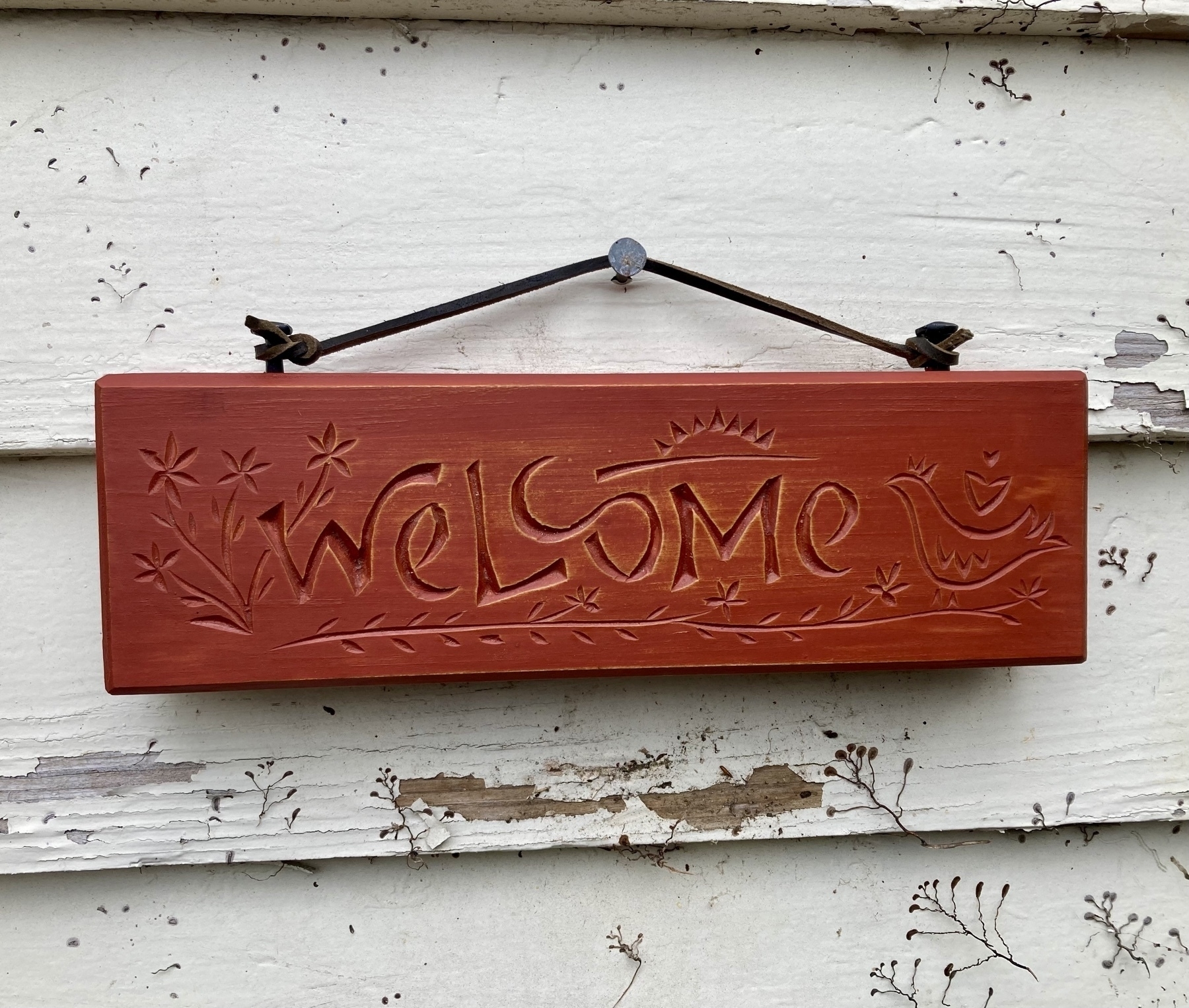 carved sign saying welcome, with a chicken and vines flowers