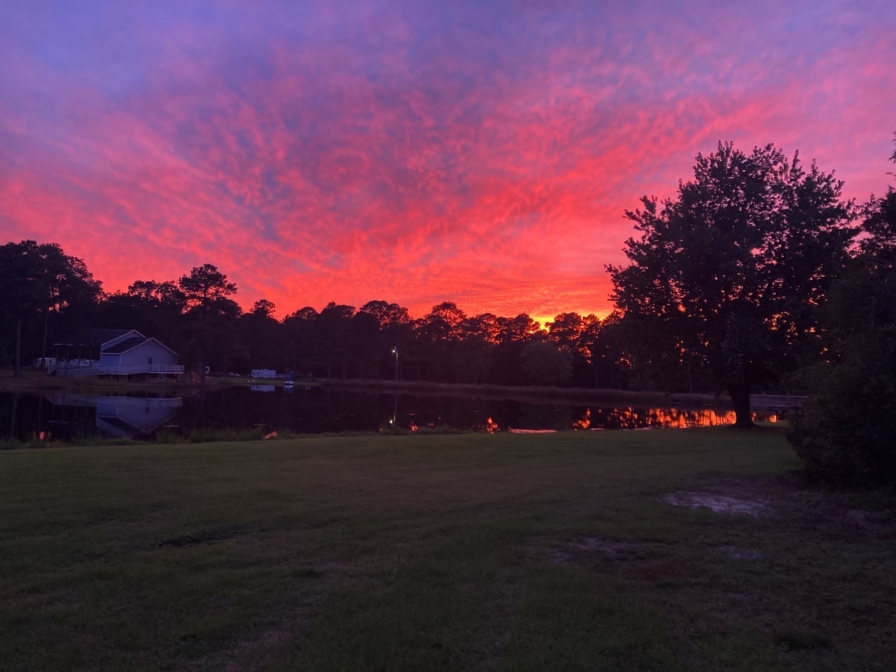 vivid orange setting sun behind trees, clouds glowing pink, reflected in lake