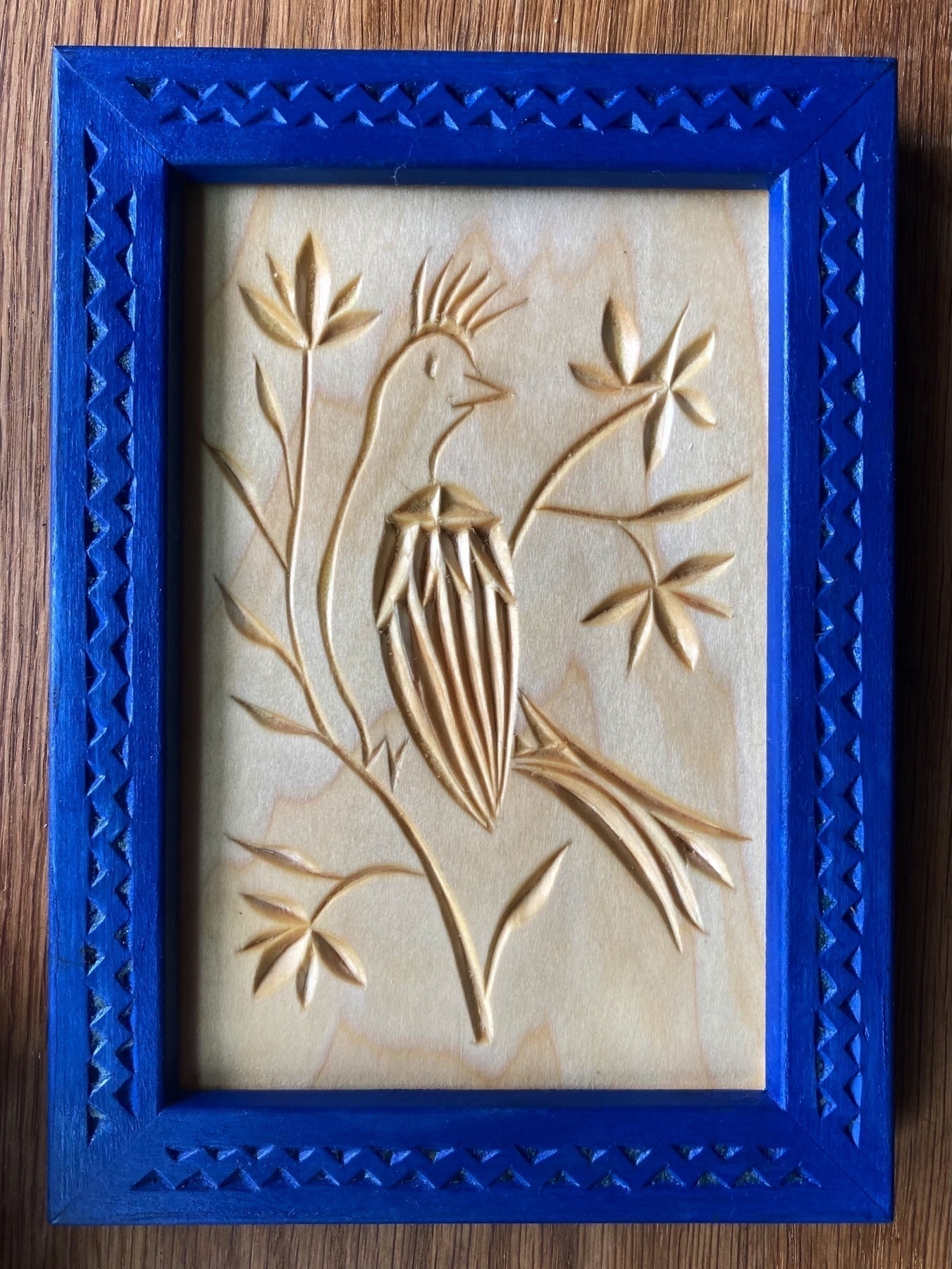 chip carving of crowned bird surrounded with flowers, blue frame carved with woven-triangle pattern