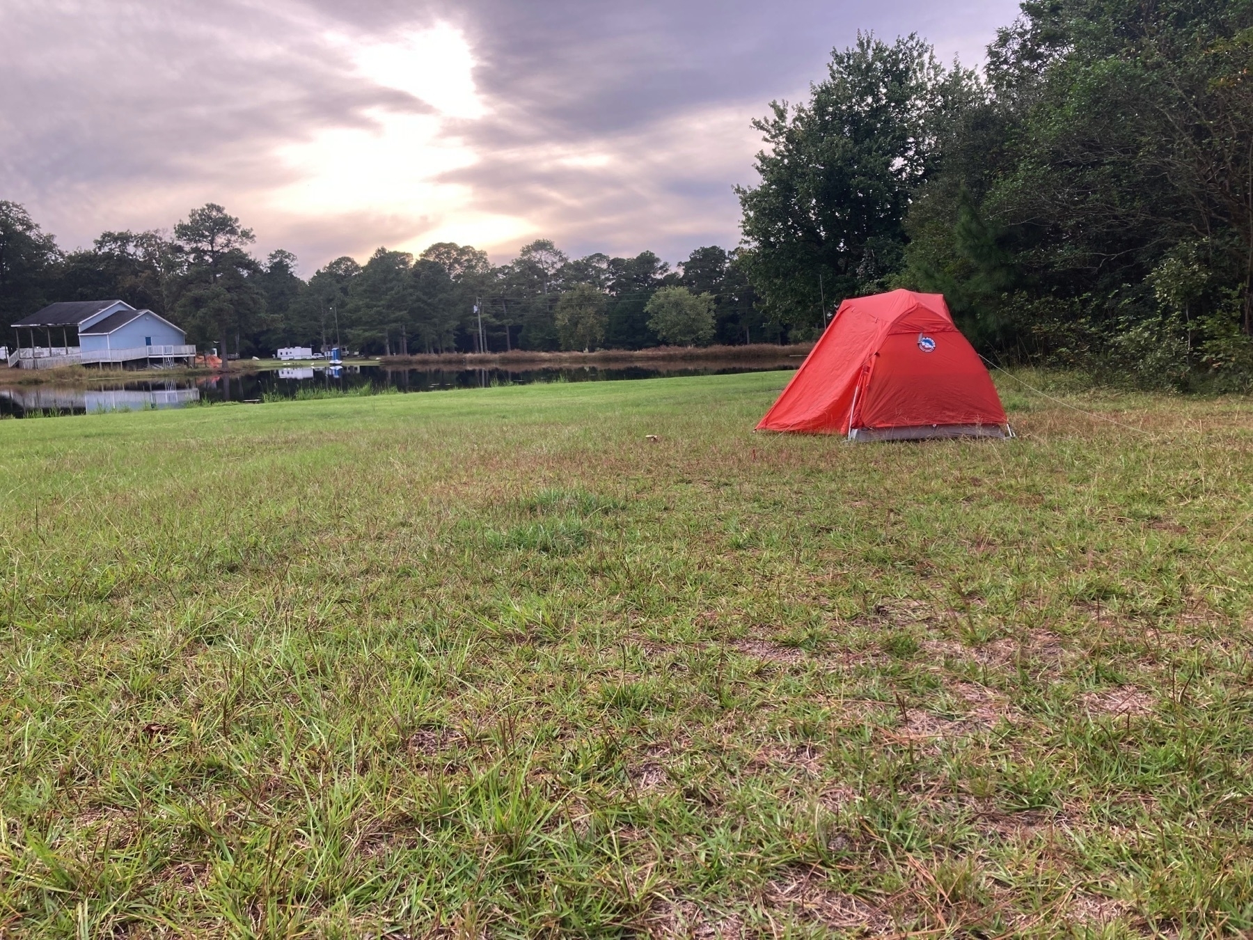 orange tent in a big field by a lake