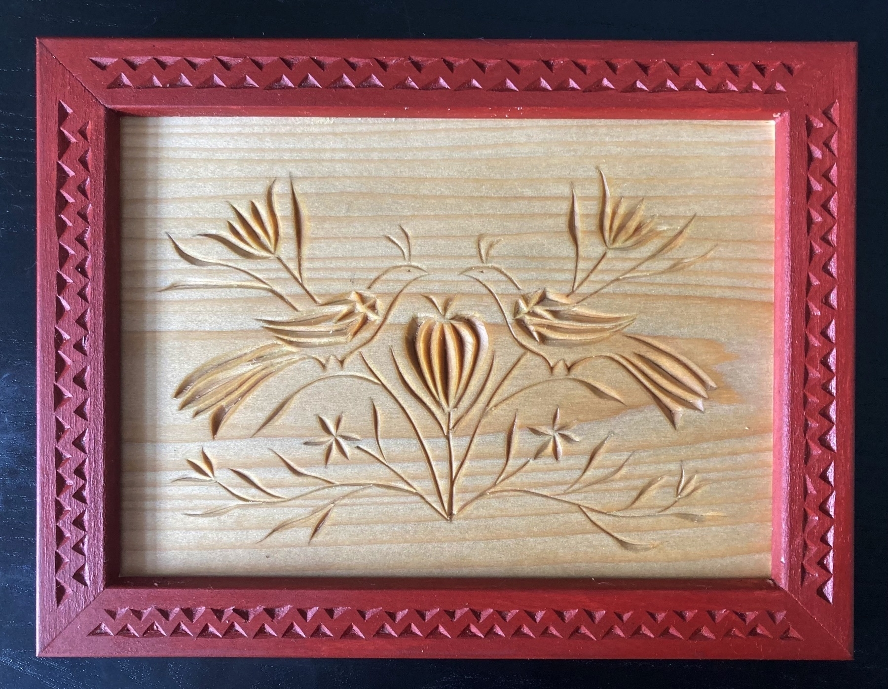carving of birds facing each other over a stylized lily; flowers protecting them; a carved frame, painted red