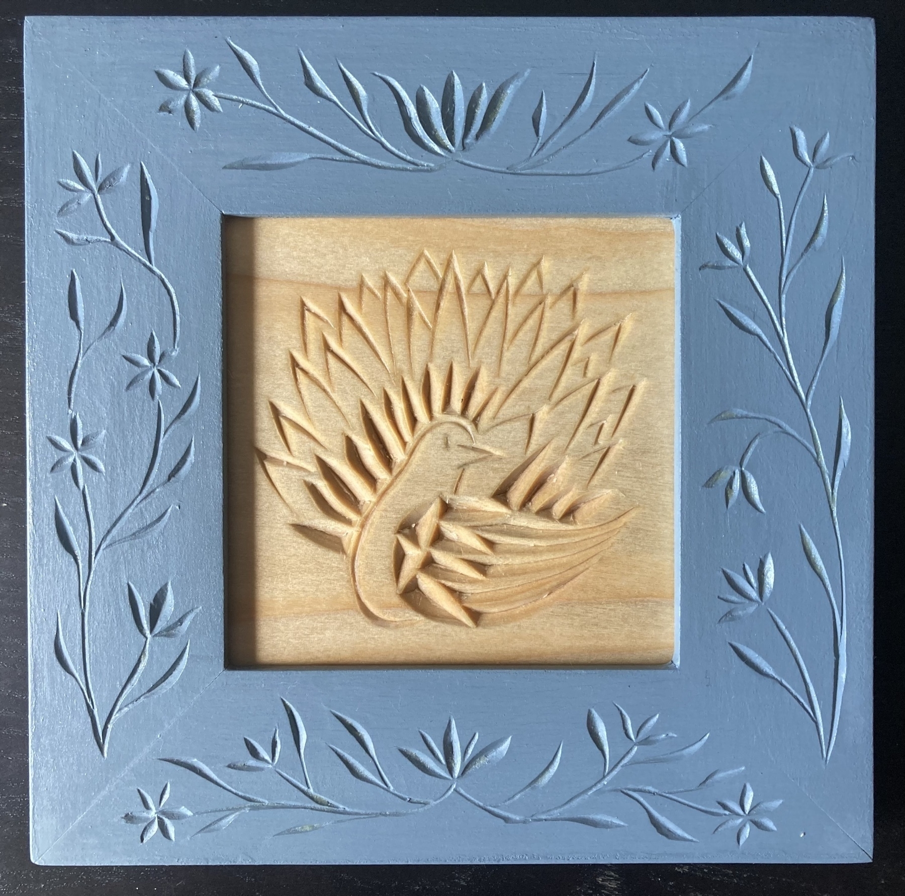 chip carving of, at least iconographically, a peacock, in a frame carved with flowers and painted light blue