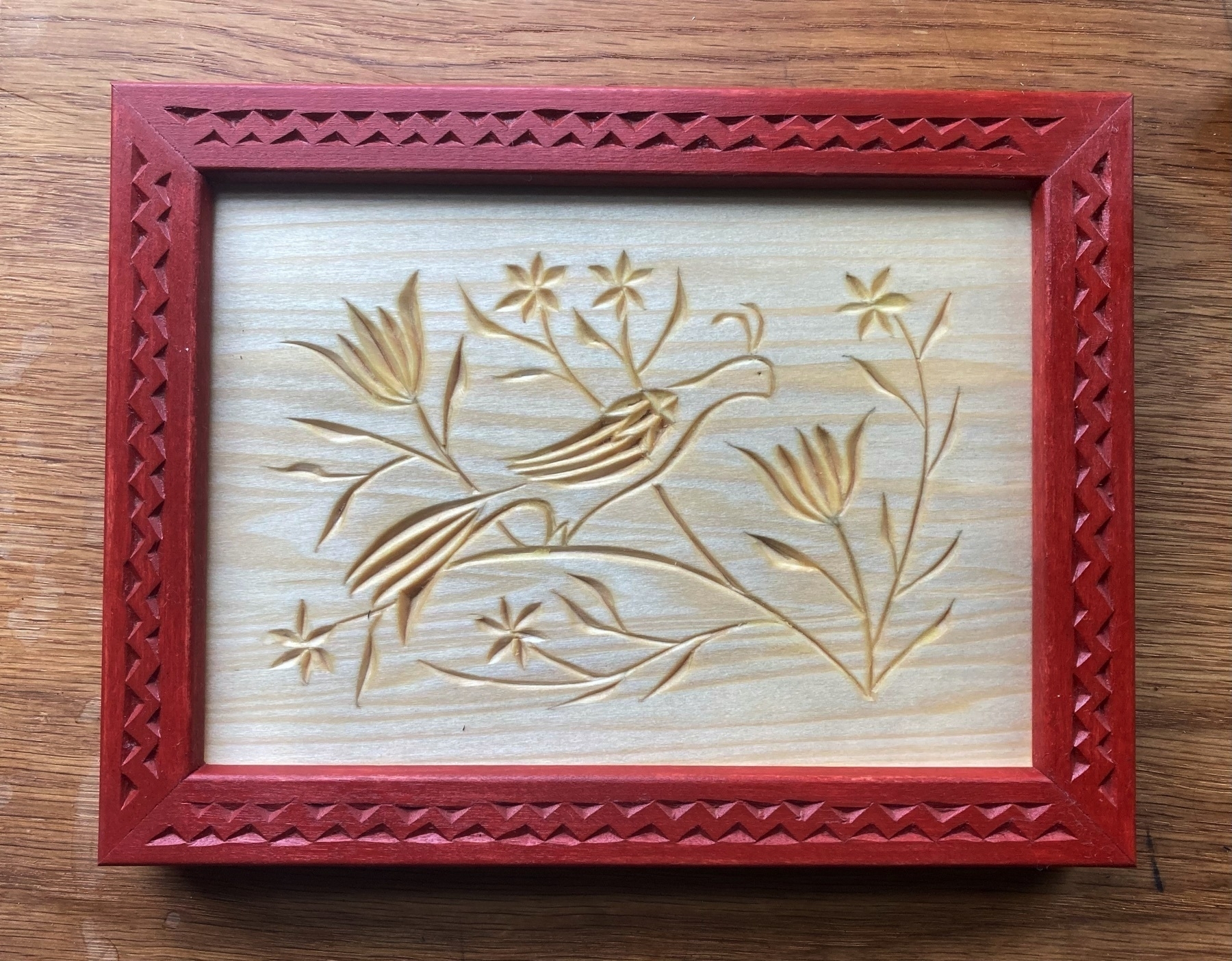 chip carving of a distelfink and tulips with red-painted chip-carved frame