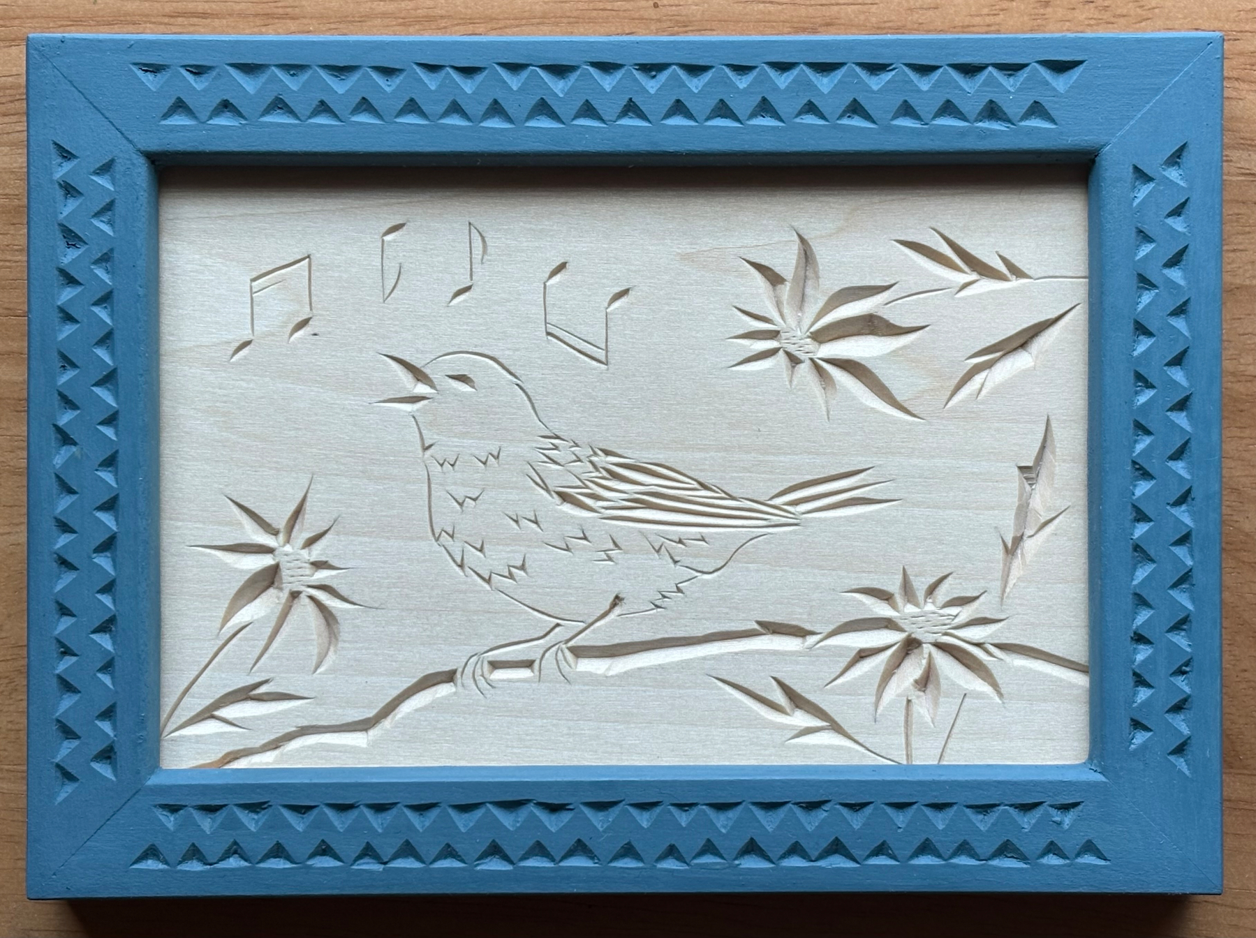 Chip carving of a bird singing on a branch, with flowers and music notes
