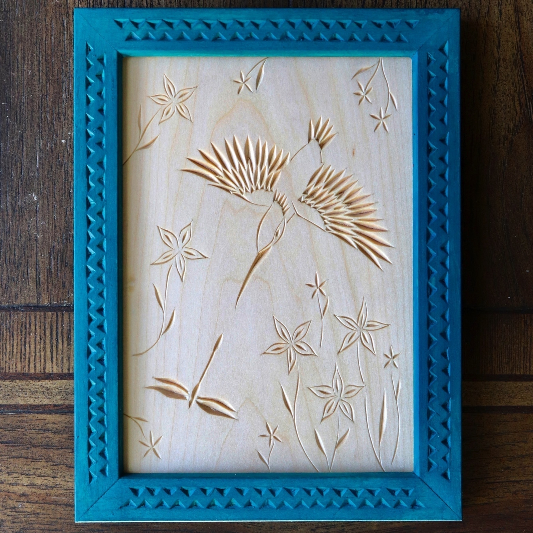 chip carving of kingfisher diving after dragonfly, with flowers; teal-blue frame