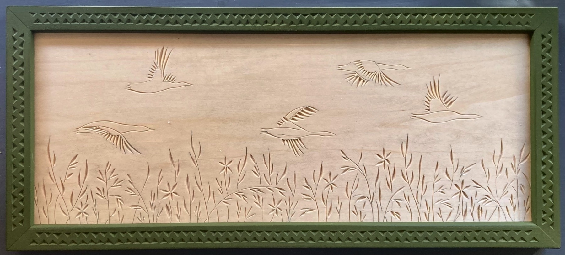 chip carving of geese flying over grassy marsh