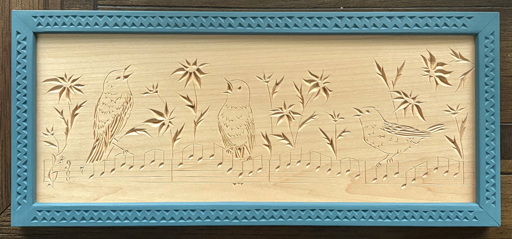 chip carving of three birds on a line of music, with flowers, blue chip-carved frame