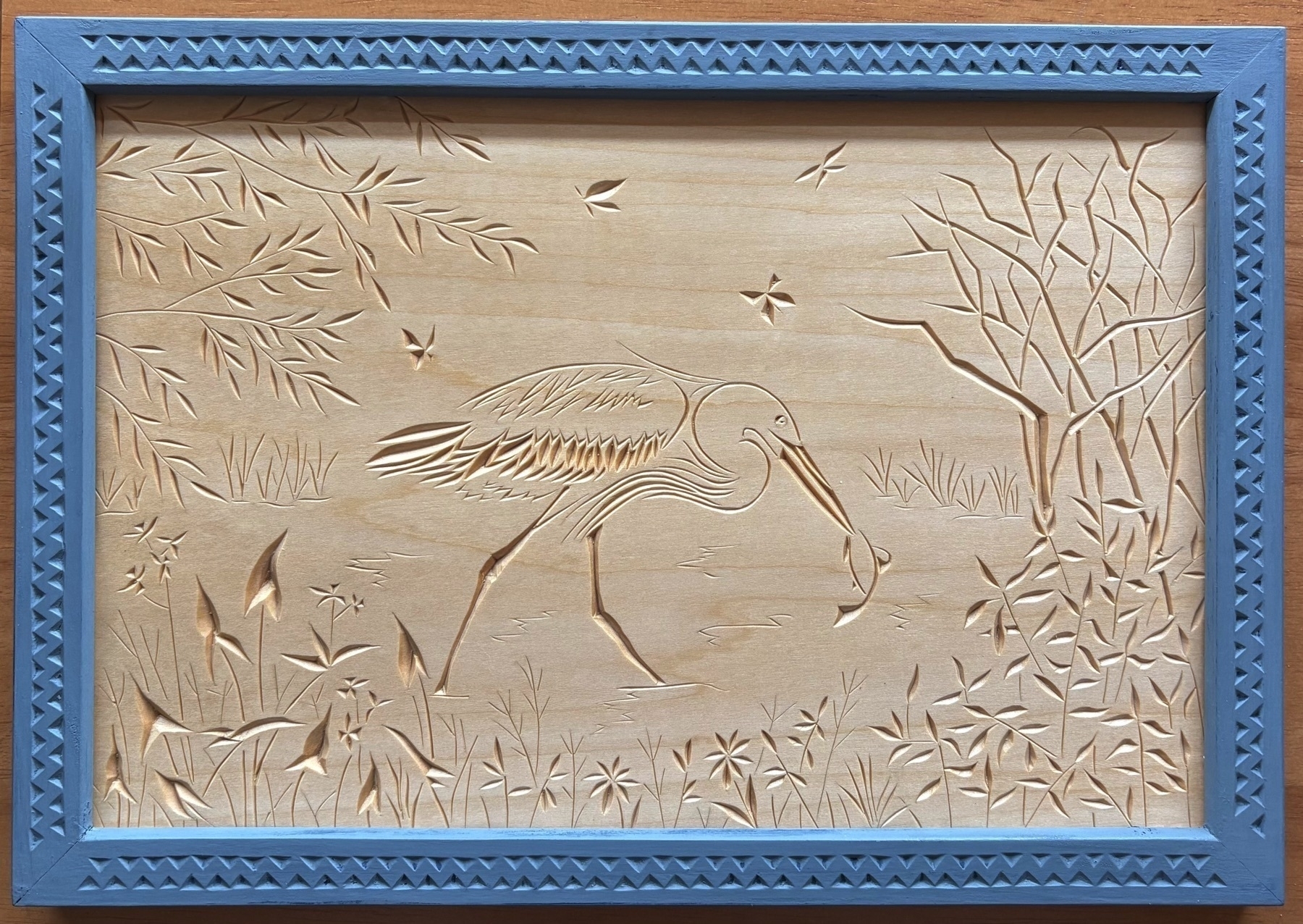 chip carving of a great blue heron amid wetland plants and trees