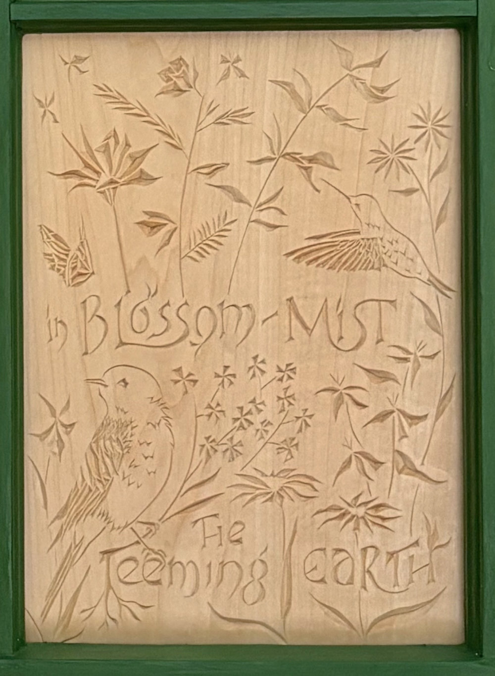 fourth panel of carving. Text reads "In blossom-mist the teeming earth," with a finch looking over its shoulder and a hummingbird among various flowers and greenery