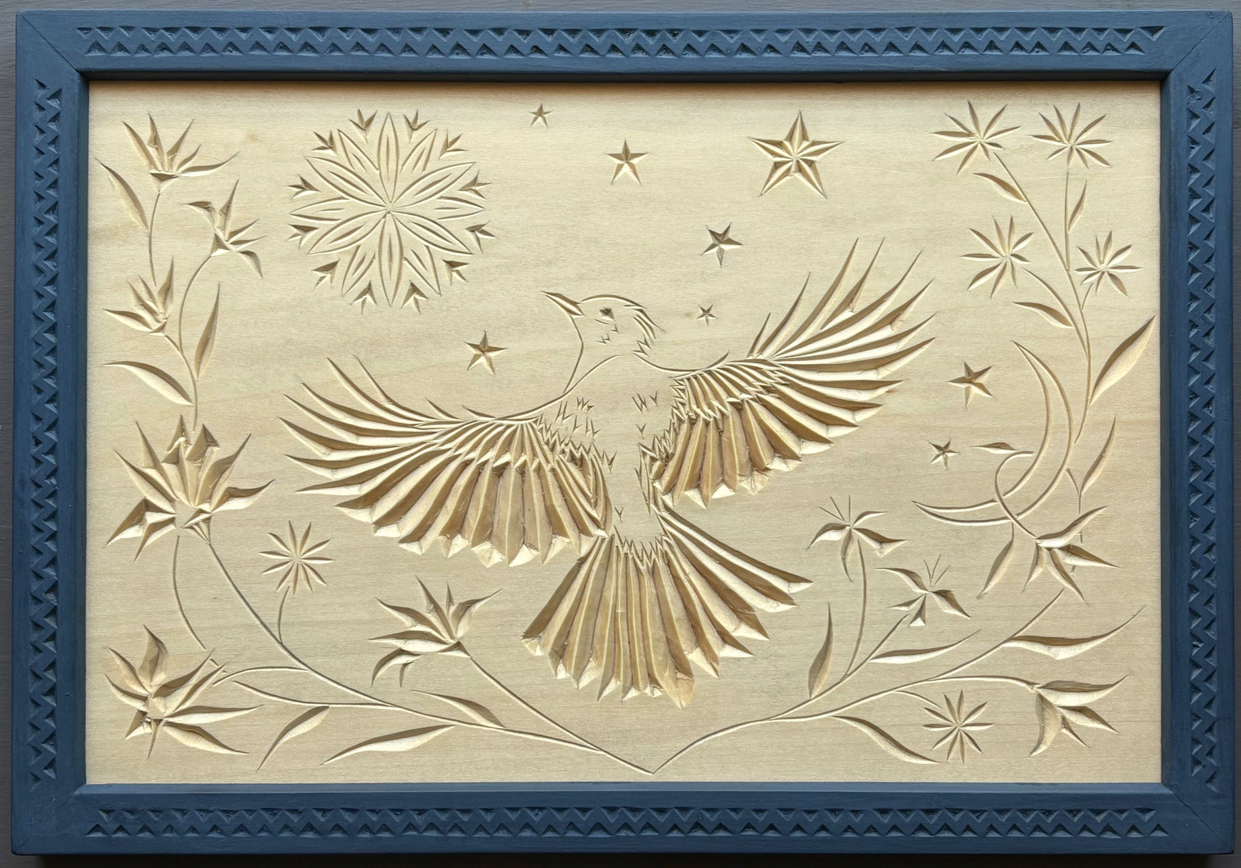 chip carving of blue jay soaring with rosette sun, moon, stars, flowers