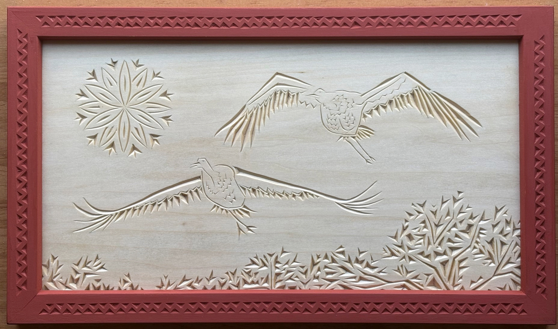 chip carving: two birds soaring over trees, with a rosette sun; frame is chip carved with geometric pattern and painted orange-red