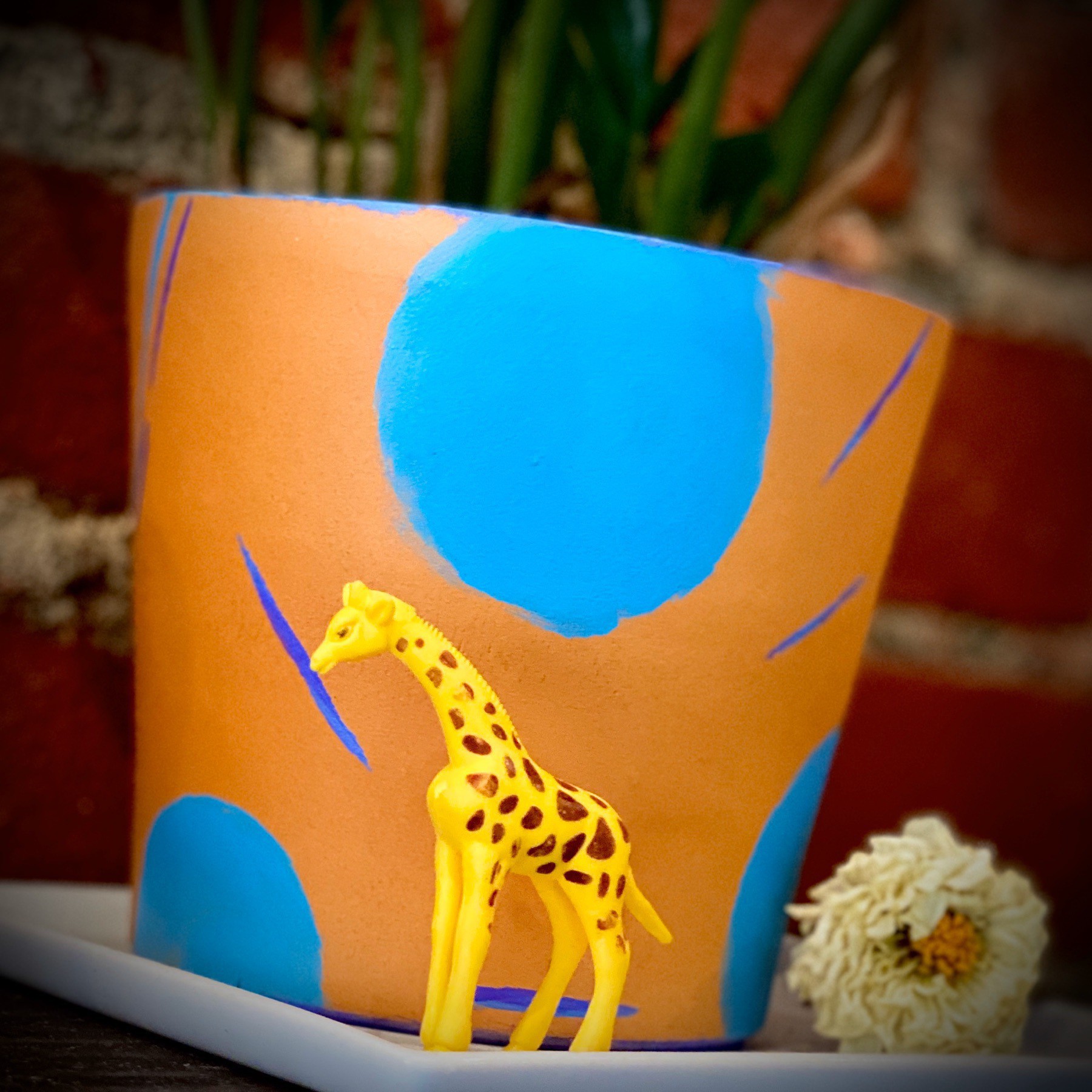 Small Giraffe figurine in front of potted plant.