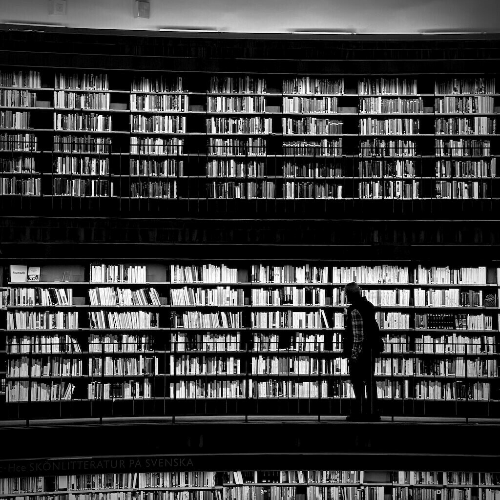Three levels of books with person in middle layer. Black and white. 
