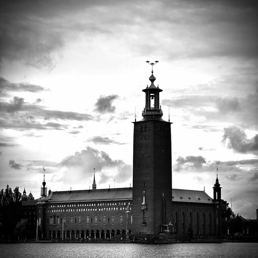 Black and white of Stockholm government building against a clouded sky.