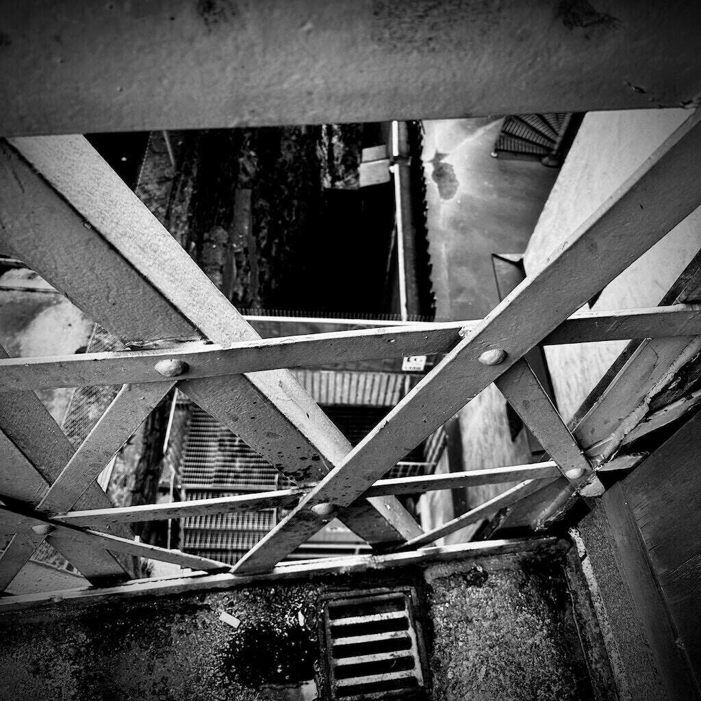 Looking down through diagonal metal girders at a staircase below. 