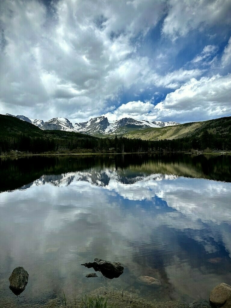 Clouded sky, hills, and mountains reflected in foreground lake. 