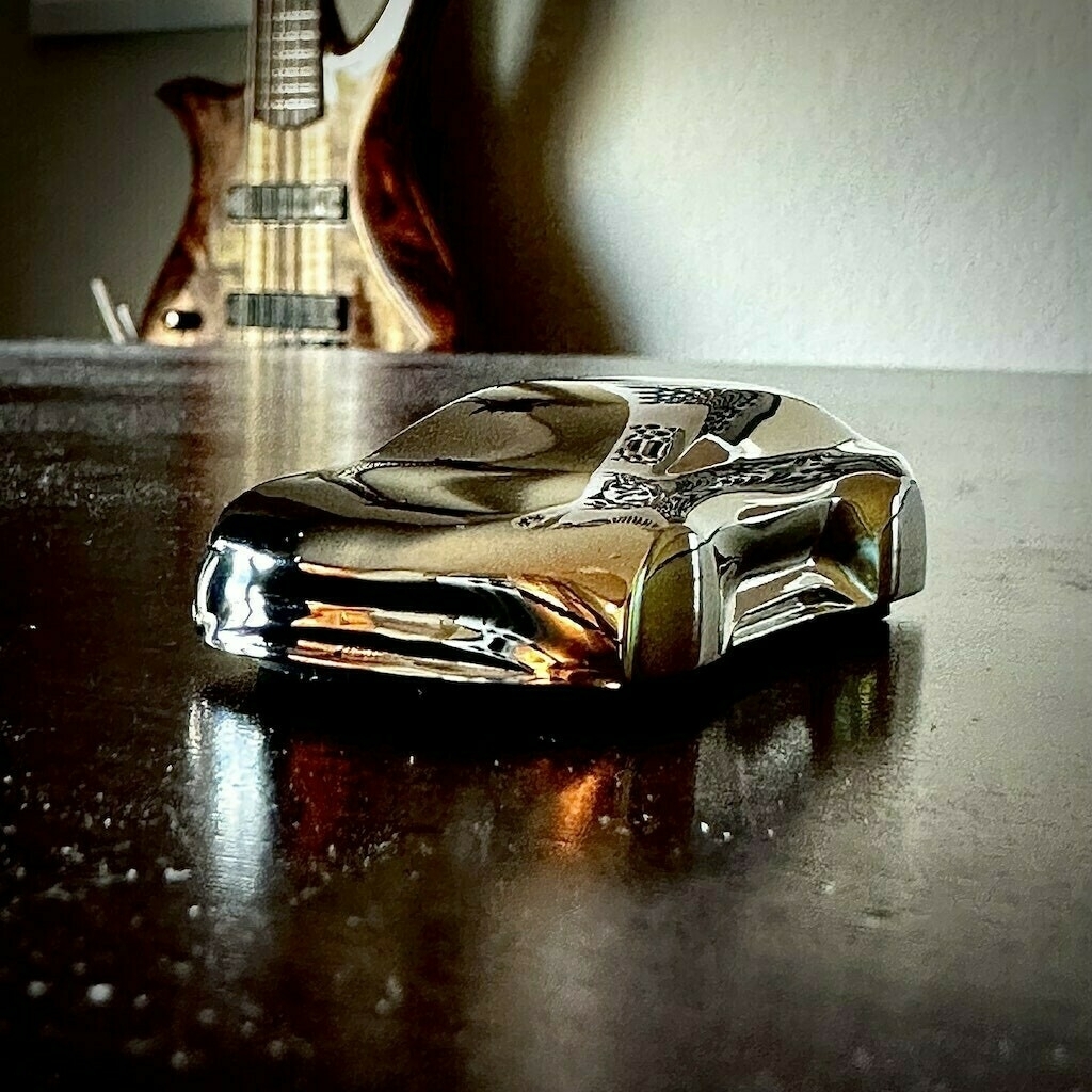 Speedform of Lucid Air in stainless steel on wooden desk with bass guitar hanging on a distant wall. 