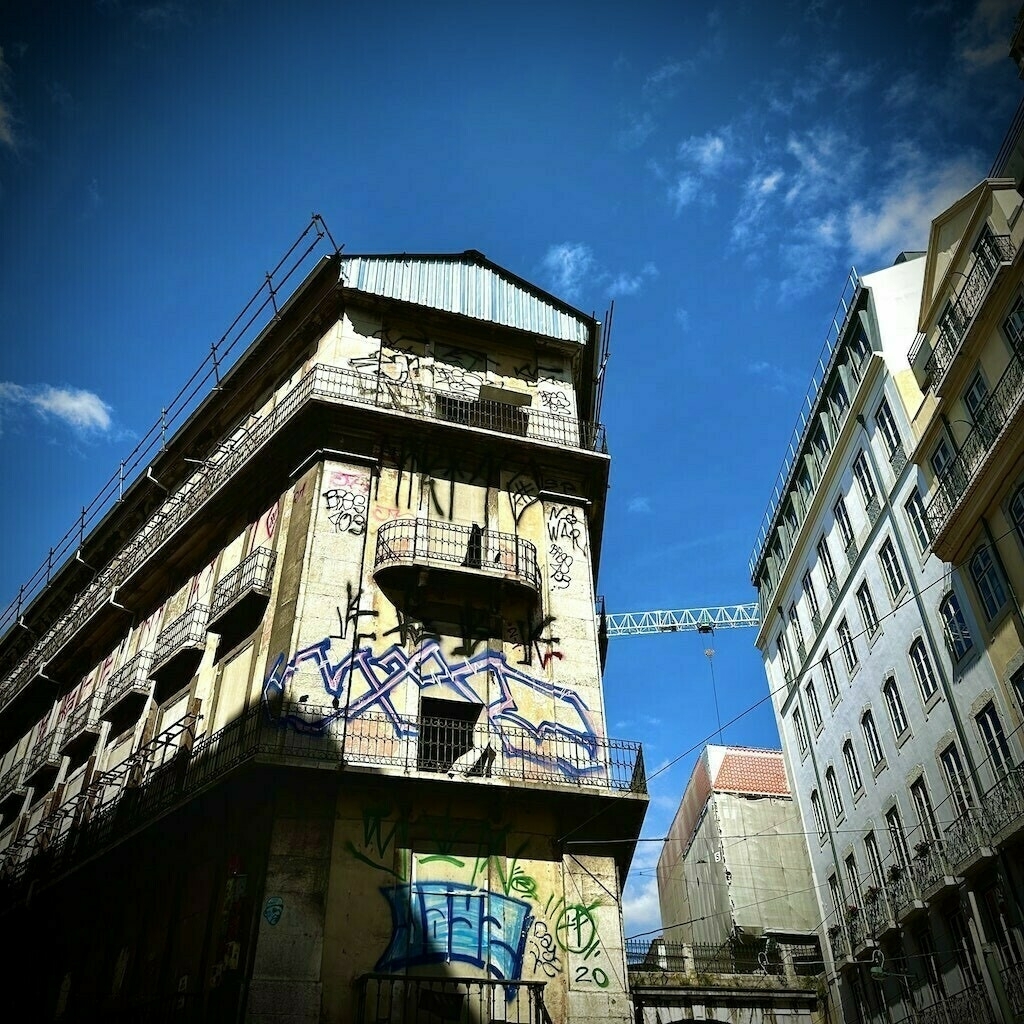 Look up at building in Lisbon, with graffiti and blue sky. 