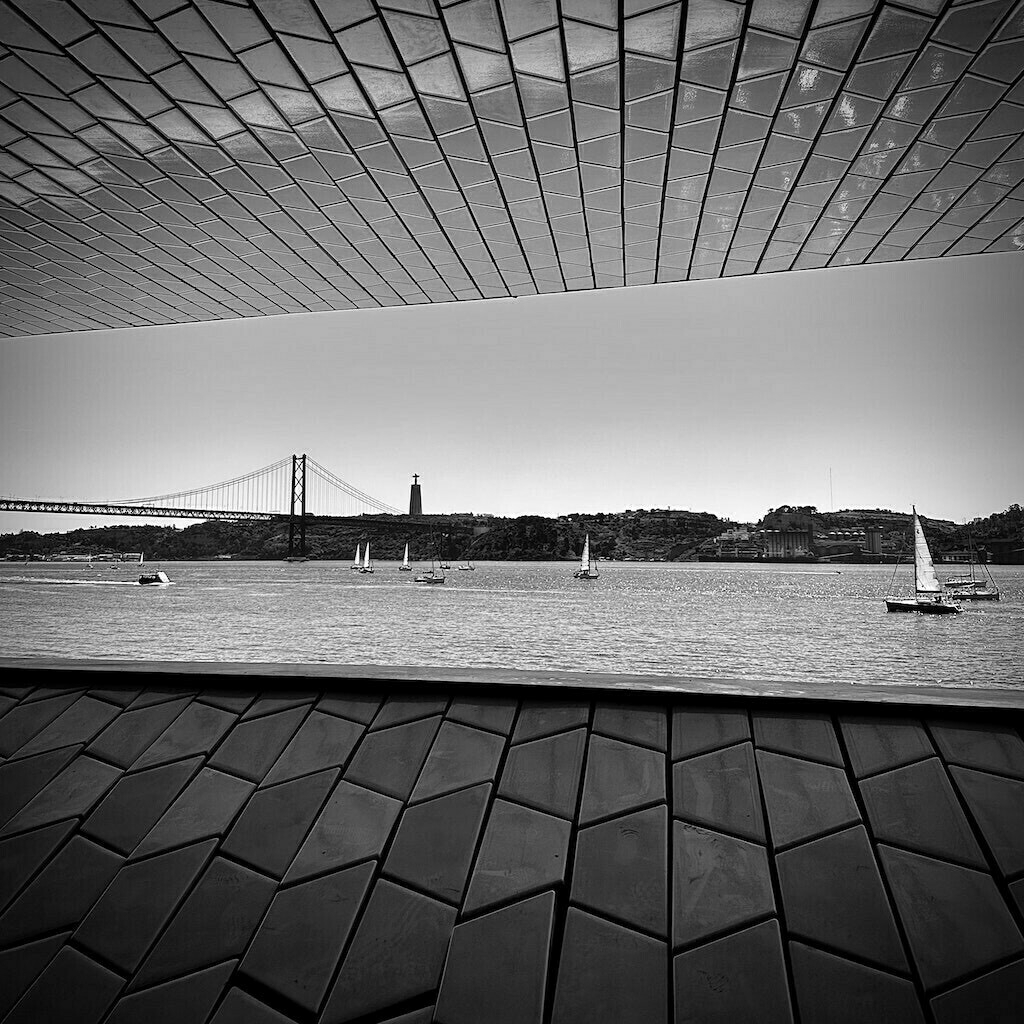 View of river, boats, and a bridge through tiled roof and wall. Black and white. 