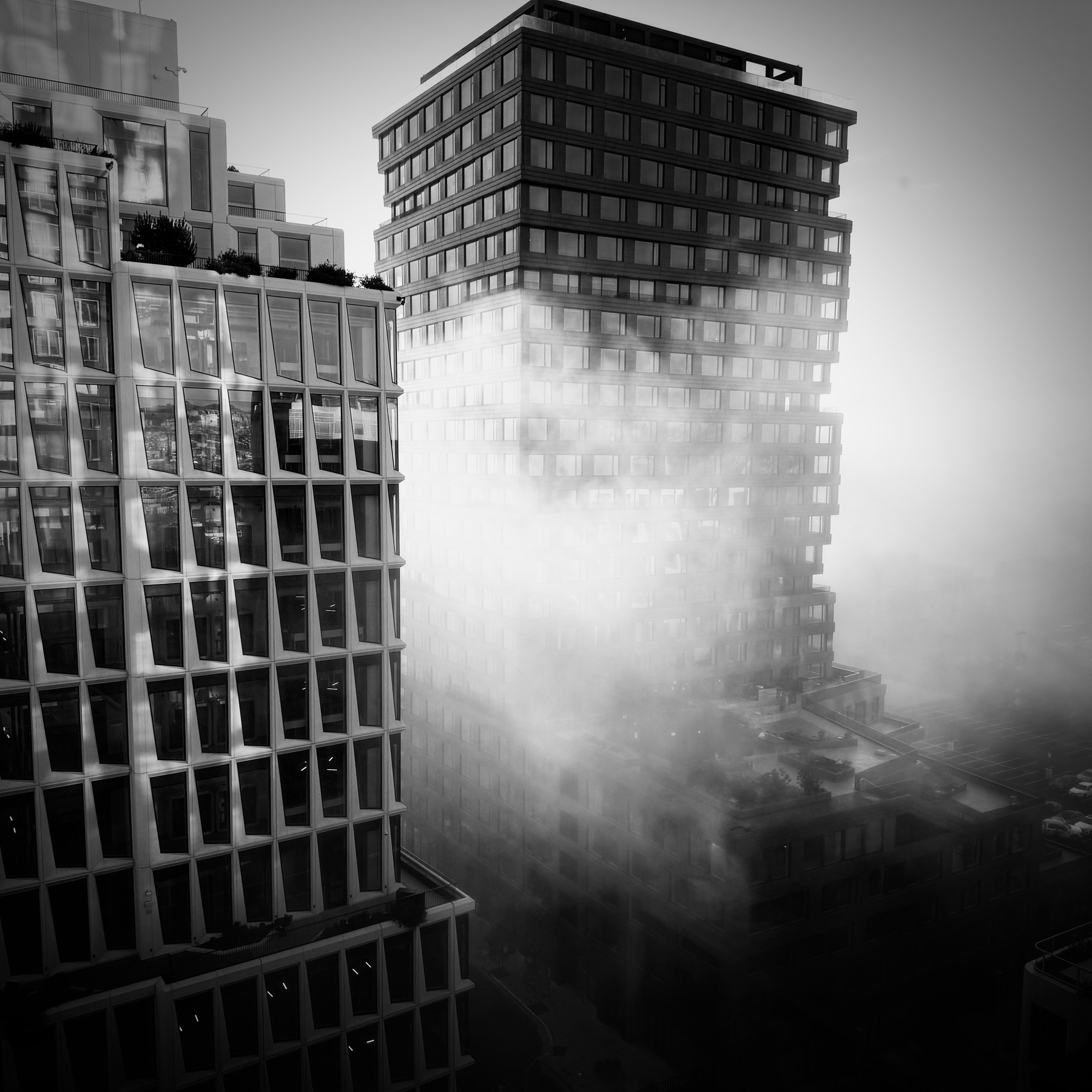 Two tall buildings with fog seeping between them. Black and White.