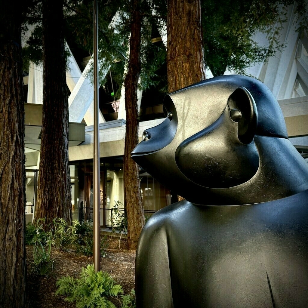 Monkey statue facing left with redwood trees and buildings in background.